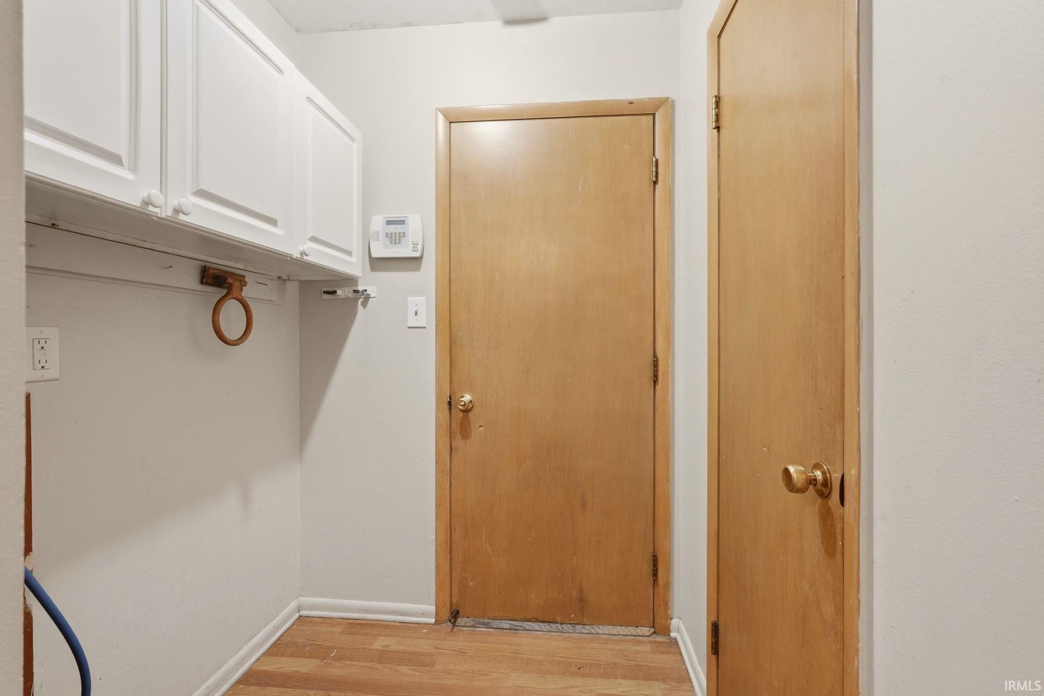 Dedicated utility space featuring overhead white cabinetry, wood-finish flooring, and light-toned walls