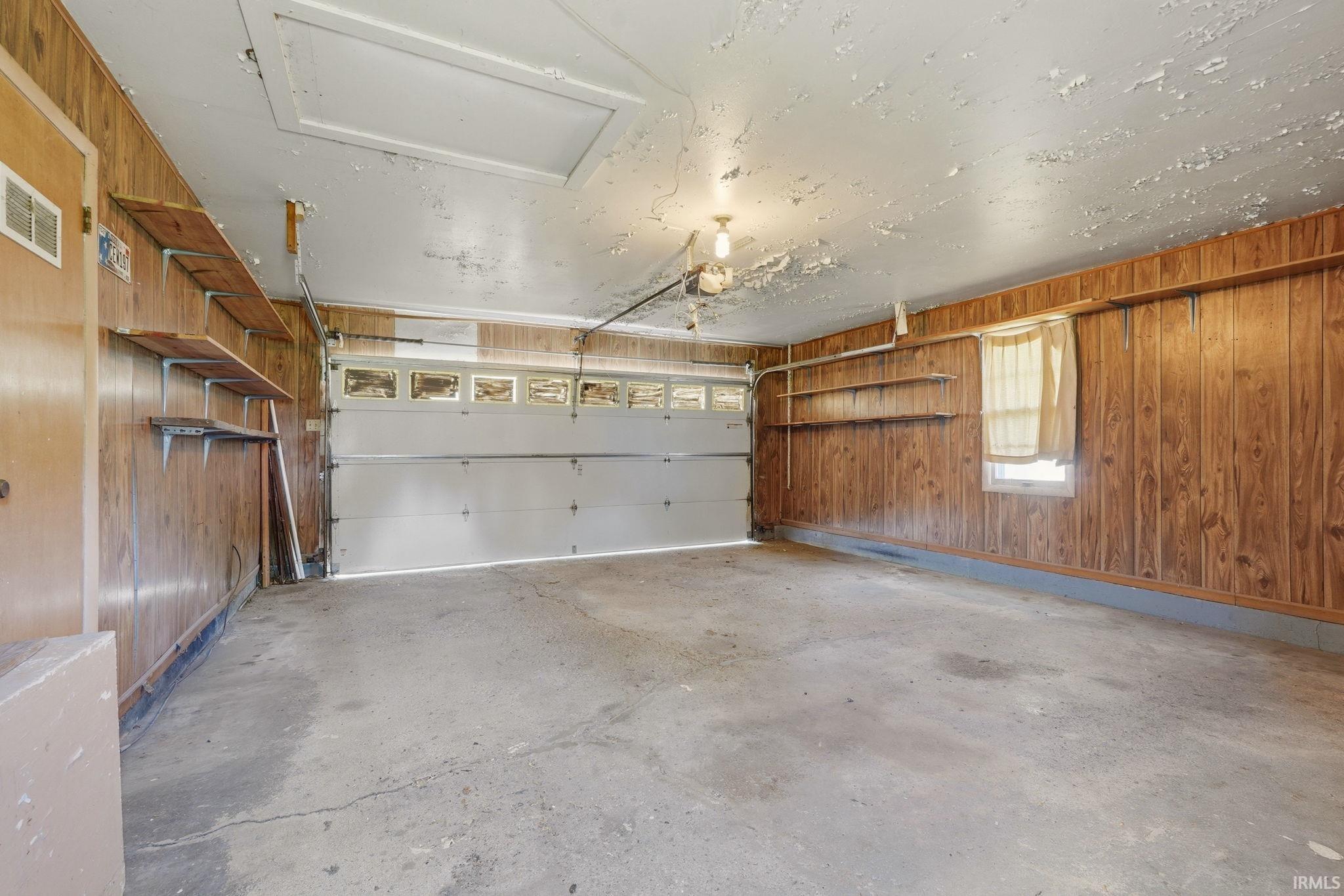 Spacious garage featuring wood paneling, a concrete floor, and overhead lighting