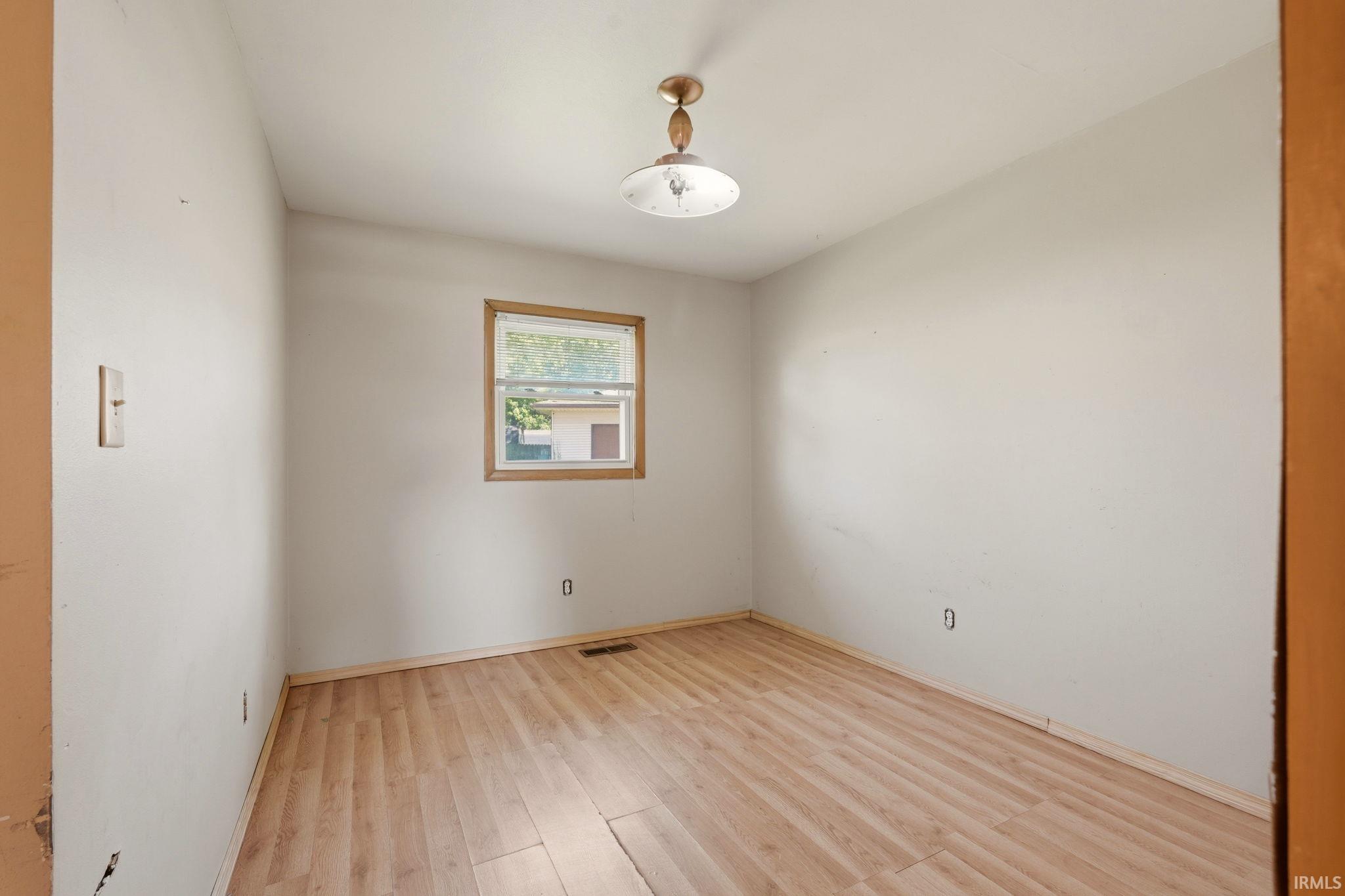 Bright room featuring wood-finish flooring, a double-hung window with wood trim, and a ceiling-mounted light fixture