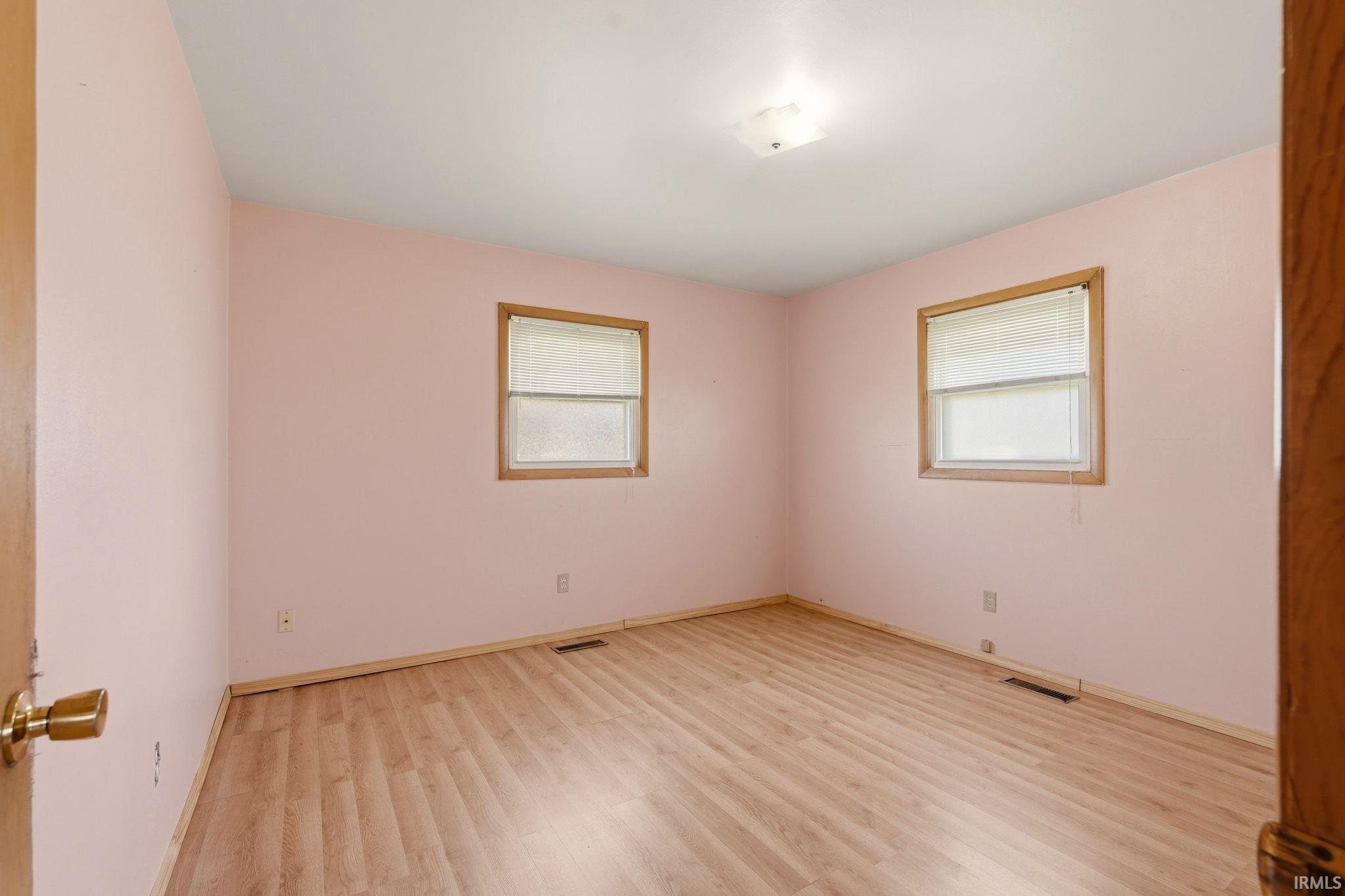 Room featuring wood-finish flooring, two windows with blinds, wood trim, and a ceiling-mounted light fixture
