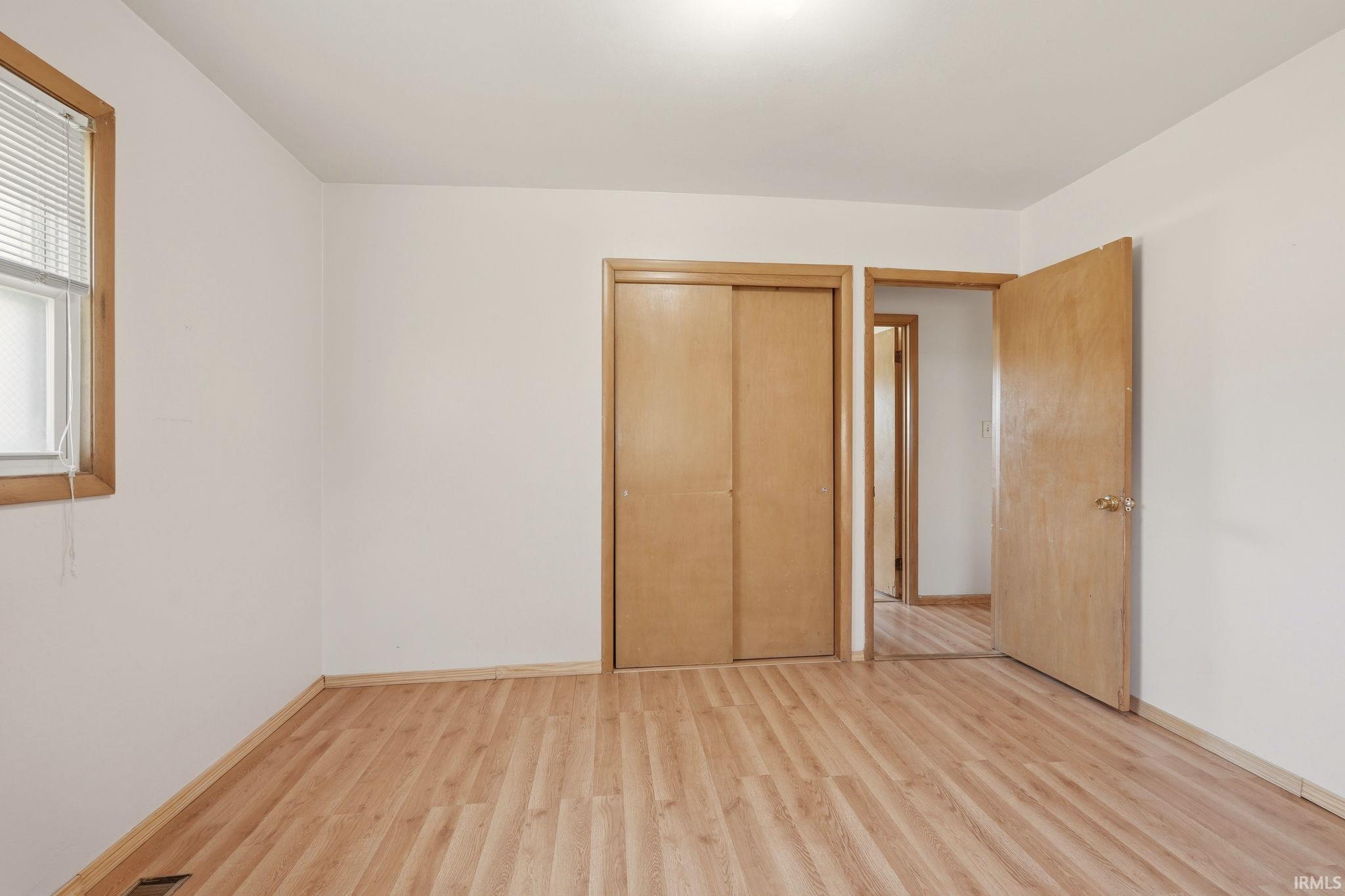 Room featuring wood-finish flooring, a double-door closet with wood panels, a window with wood trim, and a ceiling-mounted light fixture