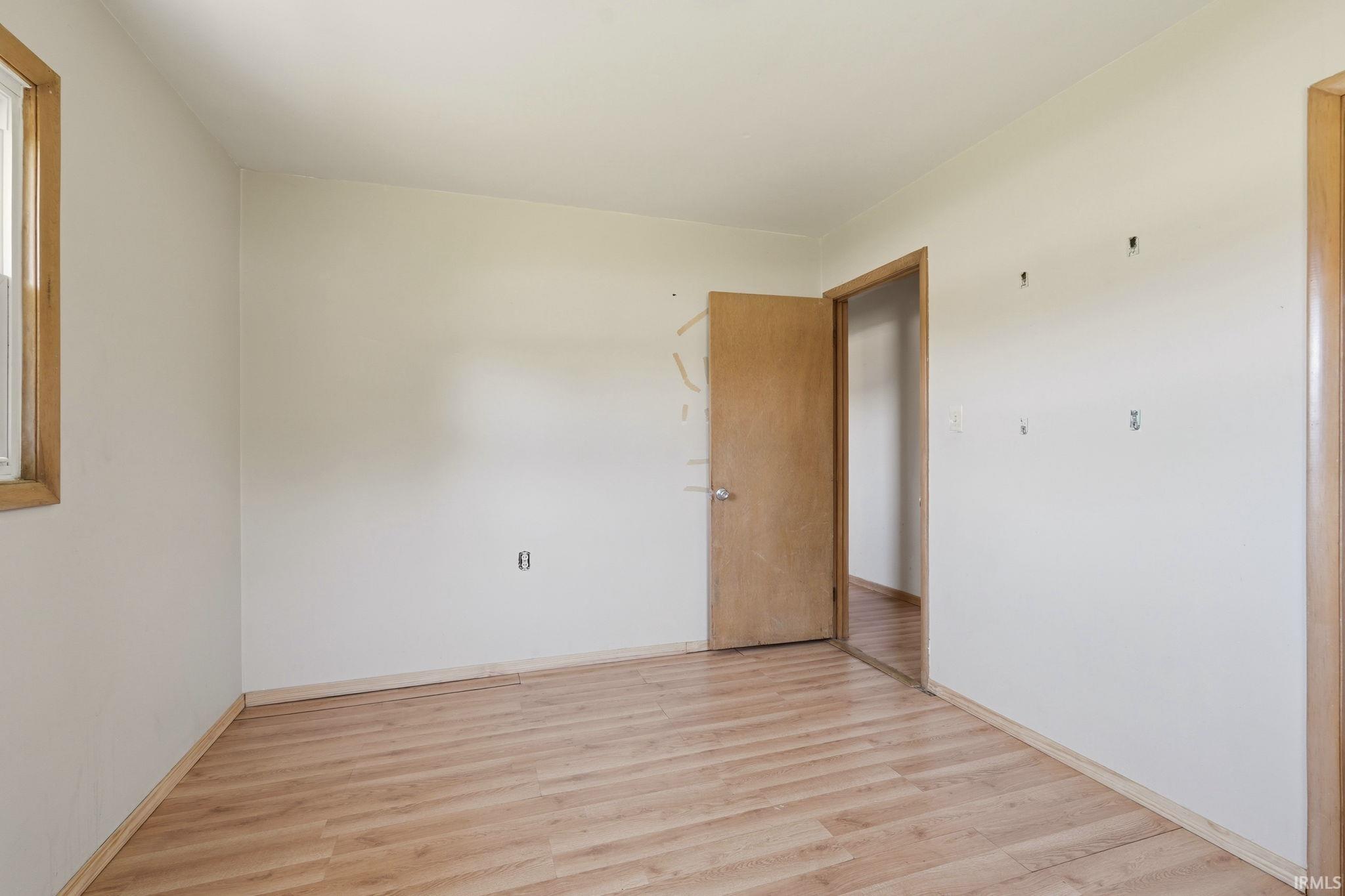Interior room featuring wood-finish flooring, a single window with wood trim, and a light-colored wood door