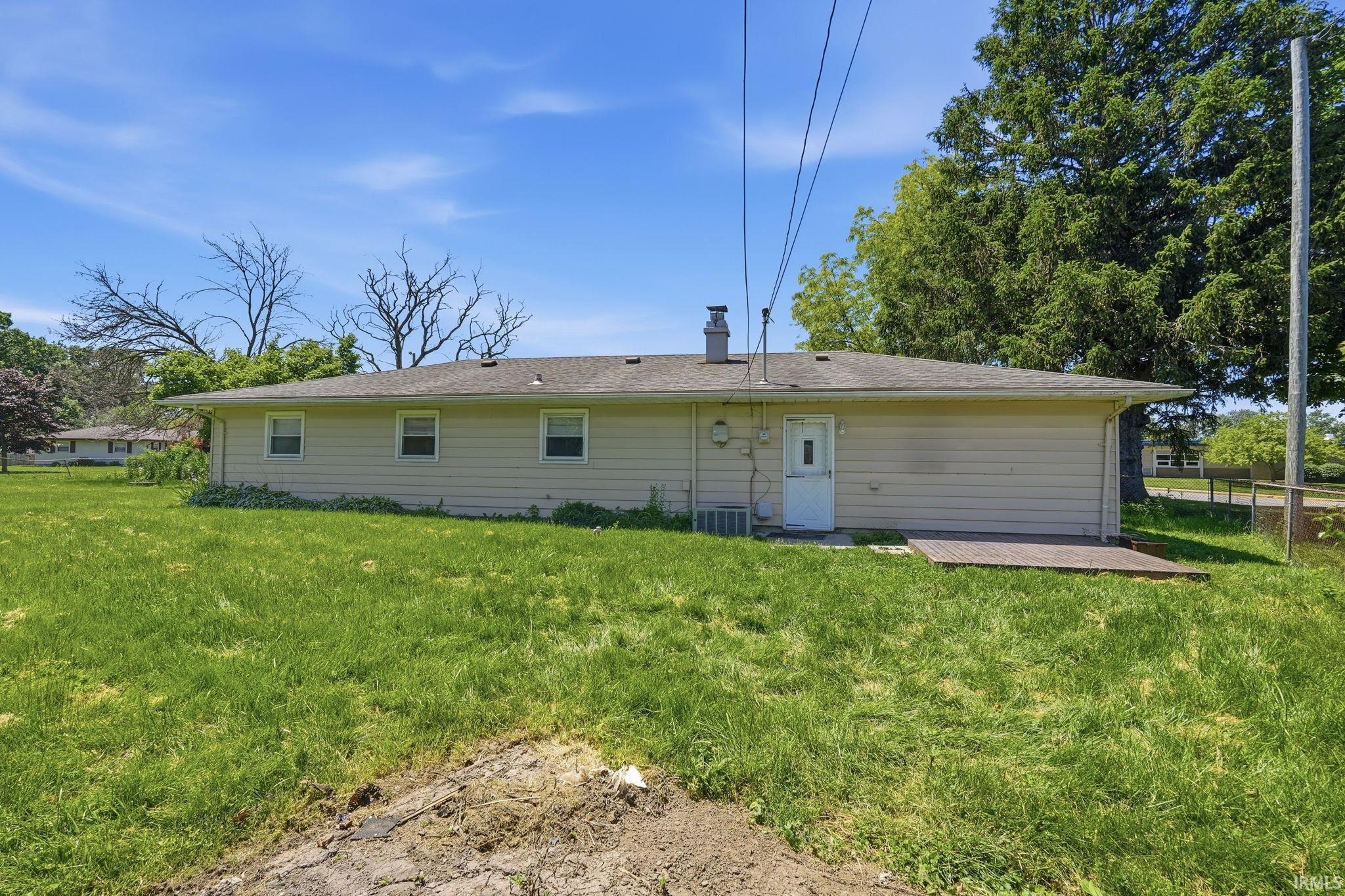Rear exterior featuring a neutral-toned siding, multiple windows, a rear entry door, and an exterior concrete pad
