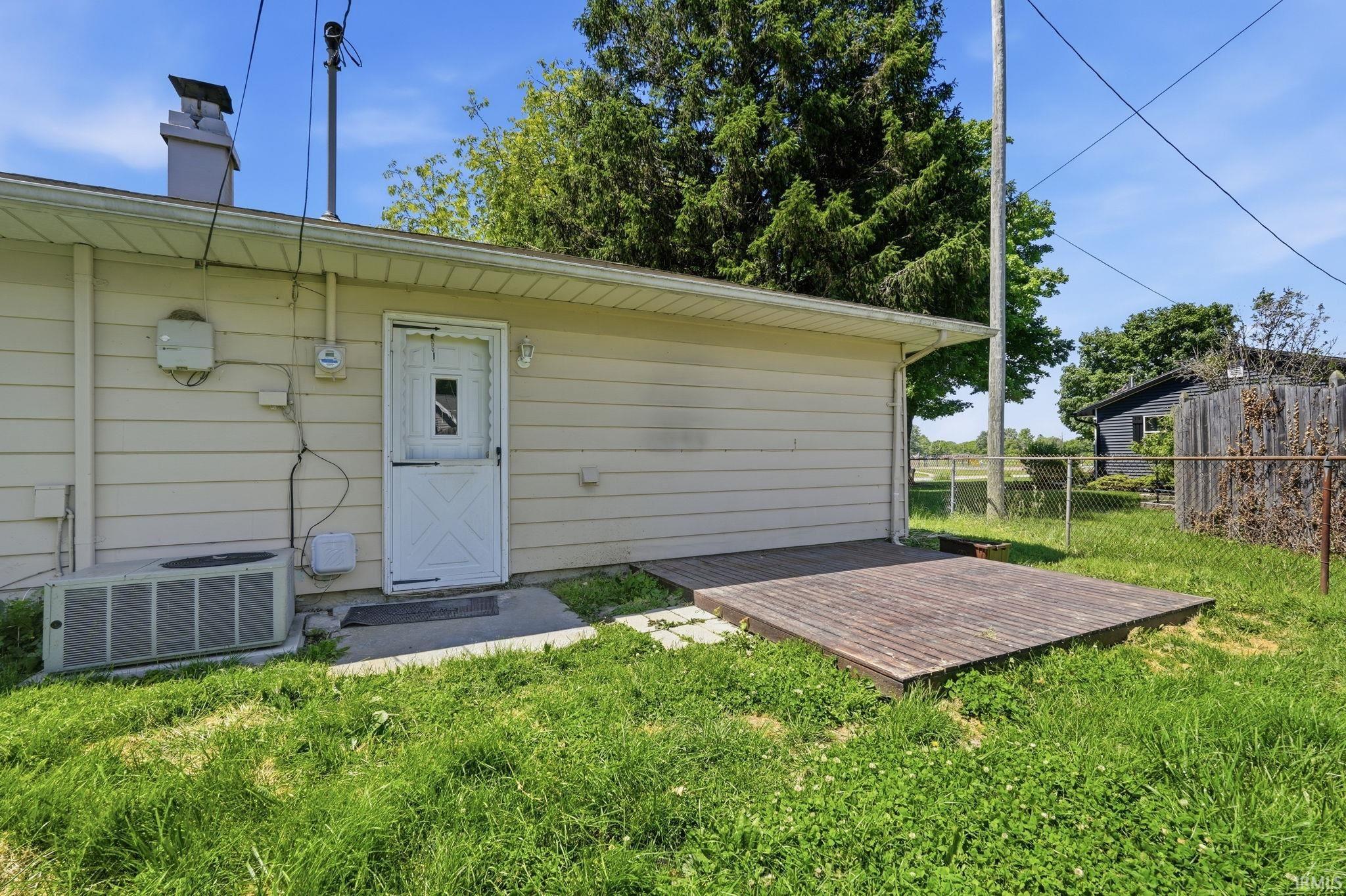 Rear exterior featuring light-colored siding, a white service door, and a built-in wooden deck