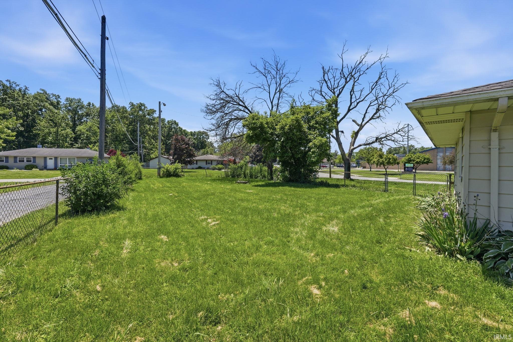 Expansive grassy yard with partial chain-link fencing, mature shrubs, and a partial view of a residential street