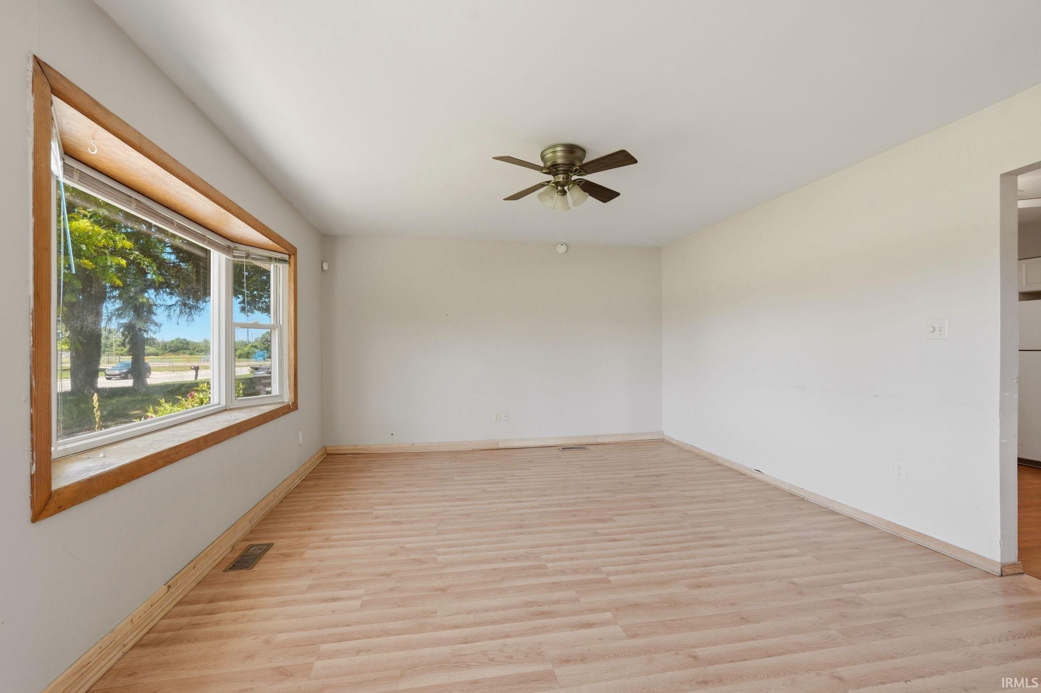 Spacious interior room featuring wood-finish flooring, a bay window with natural wood trim, and a ceiling fan with integrated lighting