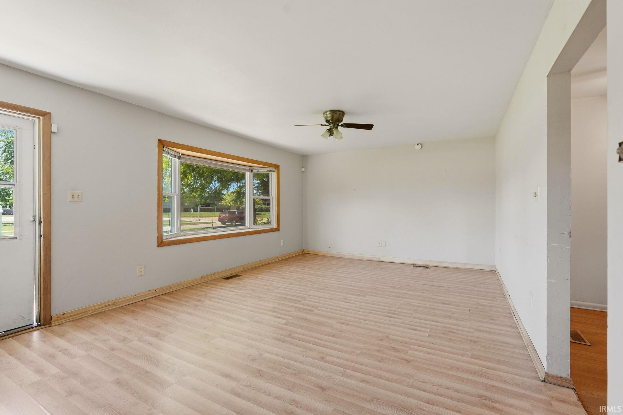 Spacious interior room featuring wood-finish flooring, a large bay window with wood trim, and a ceiling fan