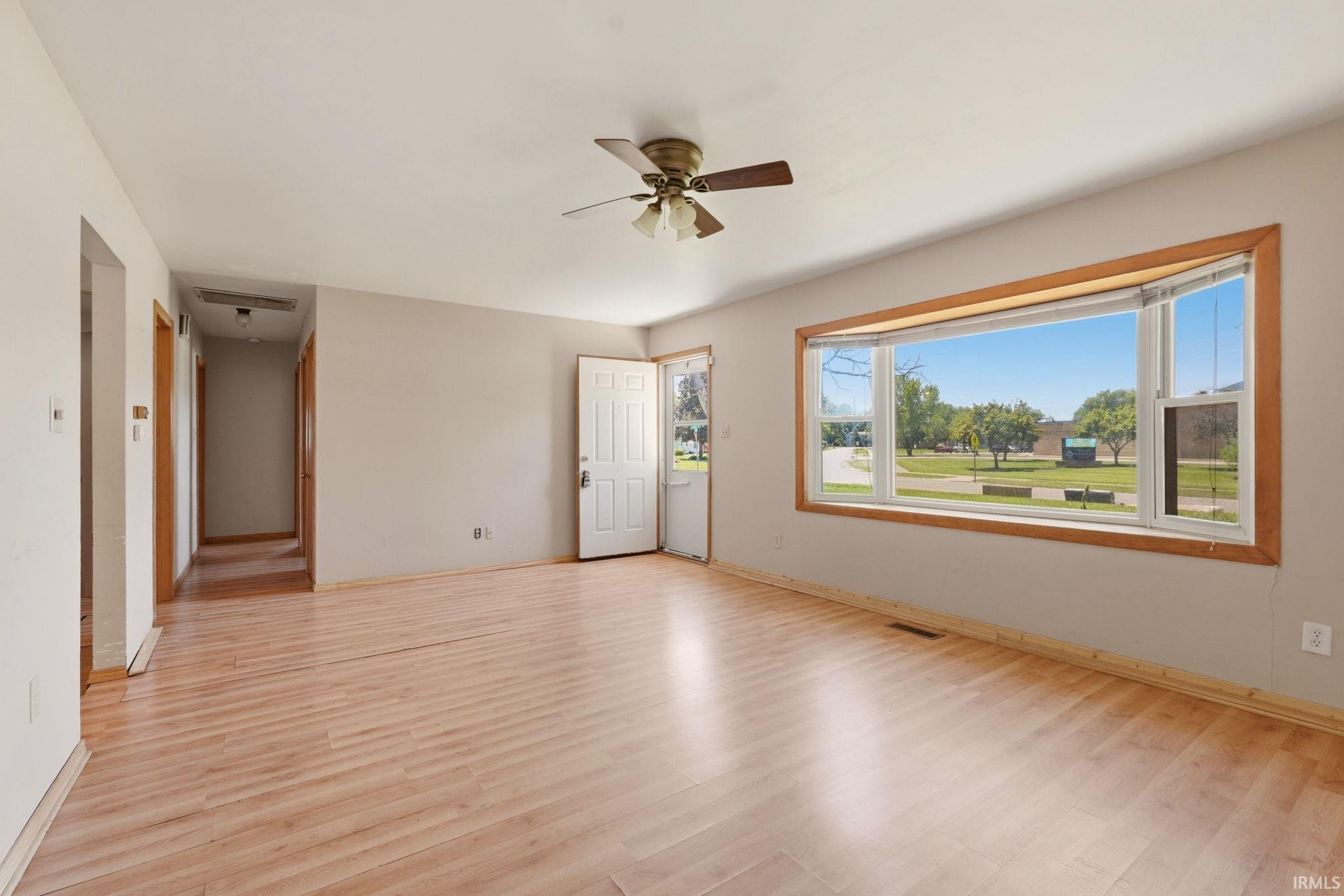 Expansive living area featuring light wood-finish flooring, a contemporary ceiling fan, and a large bay window