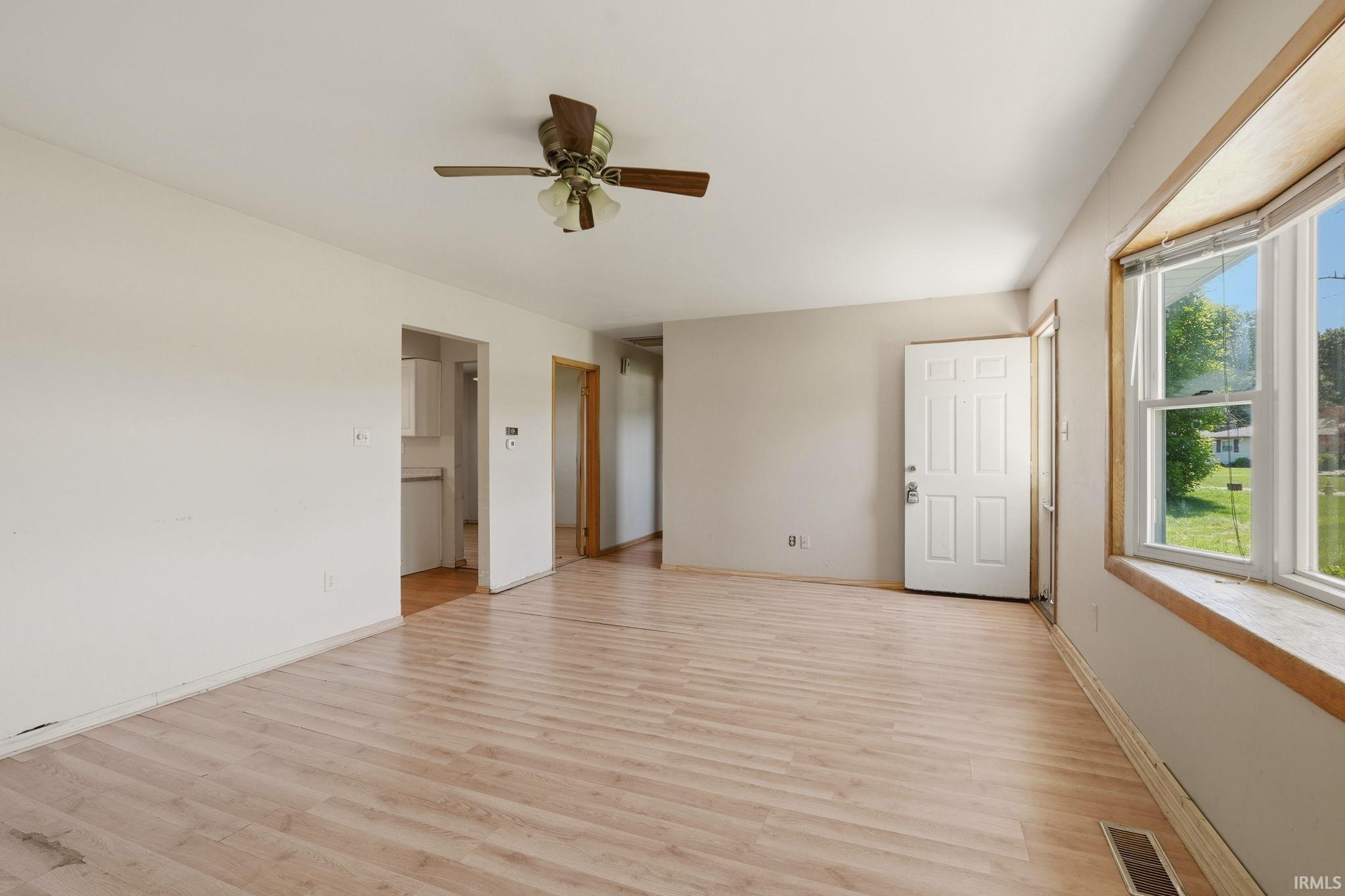 Spacious living area featuring light wood-finish flooring, a ceiling fan, and a large bay window with a wide sill