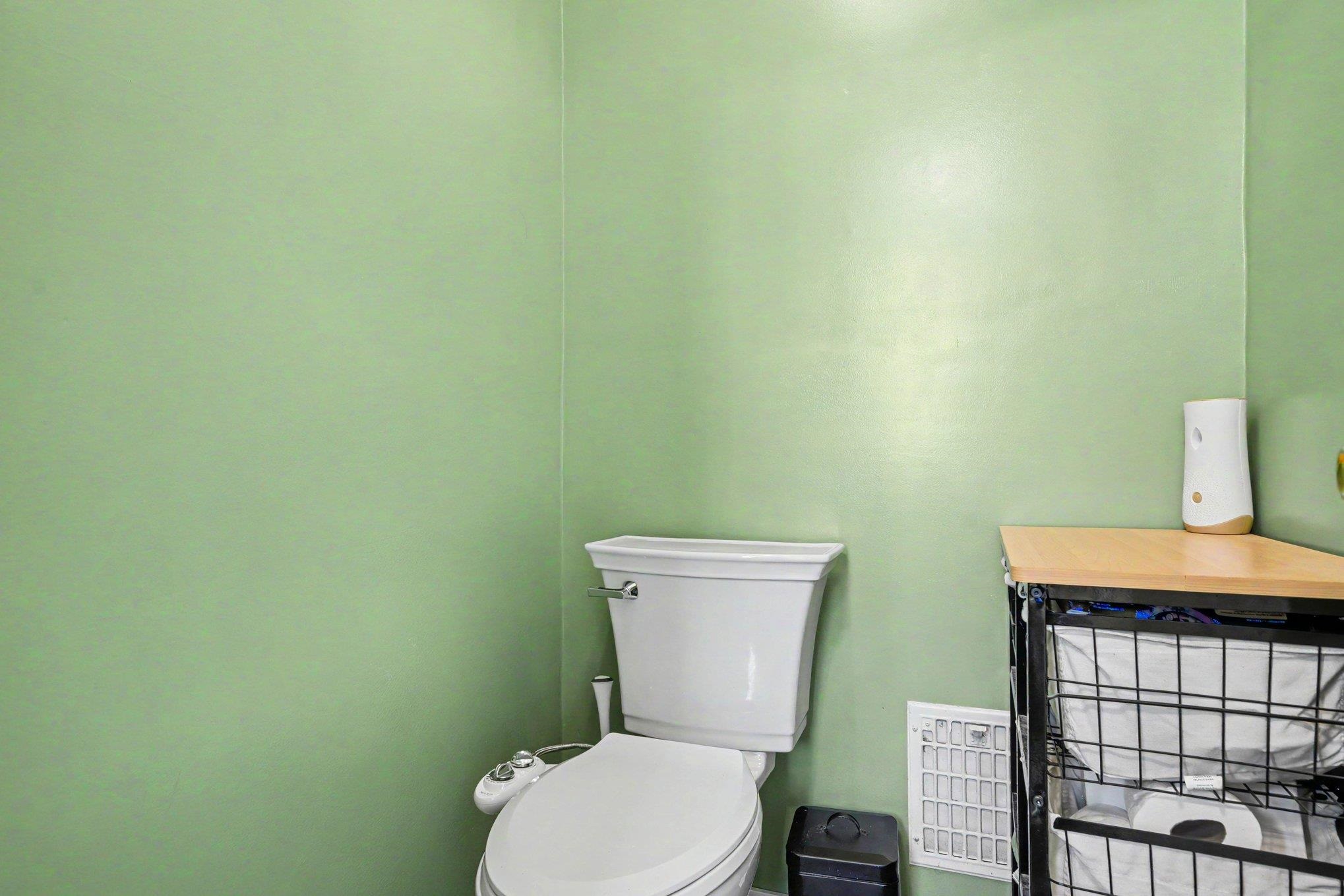 Bathroom featuring a white toilet with an attached bidet, light green walls, and a white floor vent