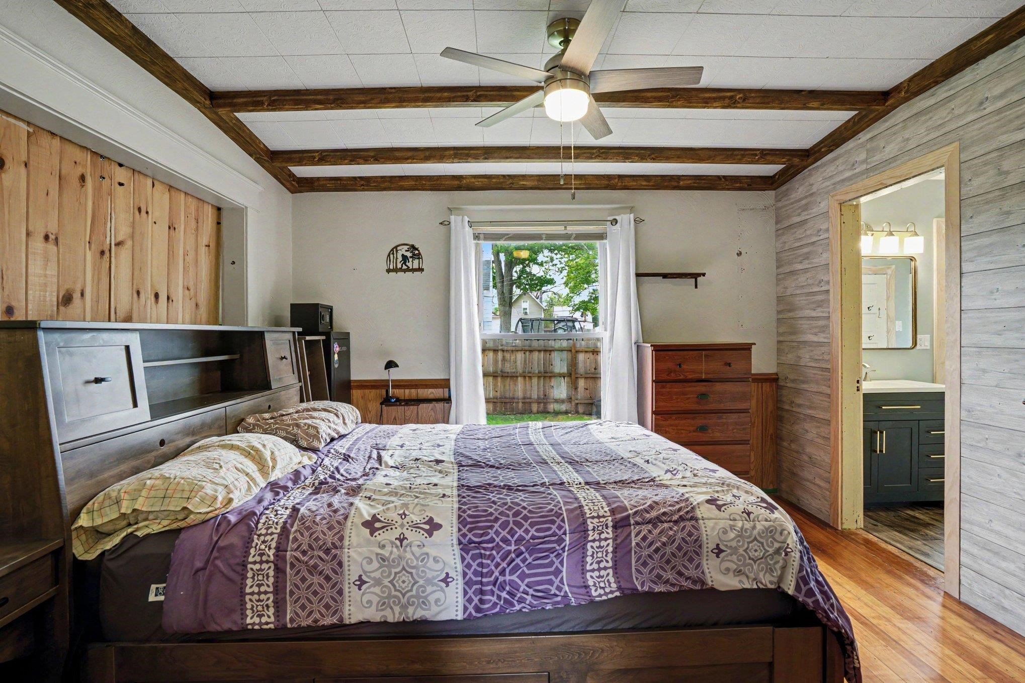Interior room featuring wood-finish flooring, a ceiling fan, exposed wood beams, and a wood-paneled accent wall