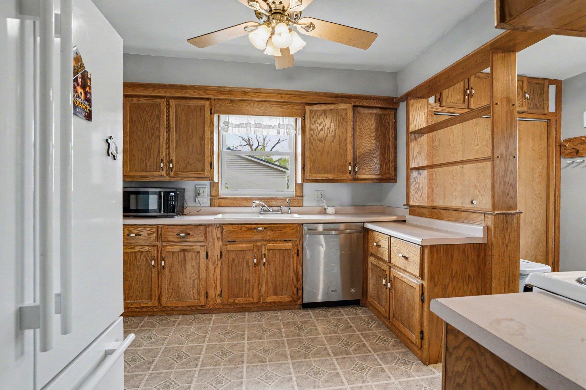 Kitchen featuring wood cabinetry, laminate countertops, a stainless steel dishwasher, and a ceiling fan