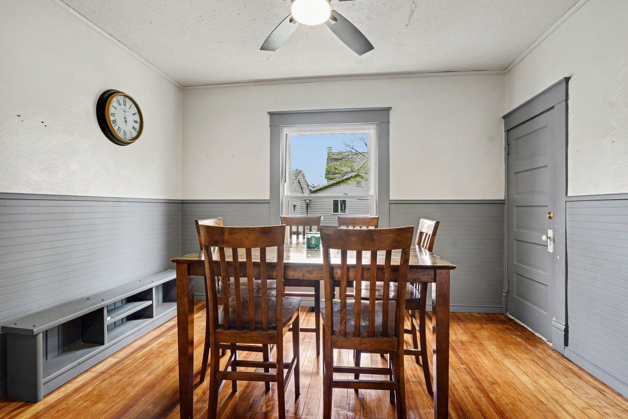 Room featuring wood-finish flooring, grey beadboard wainscoting, and a ceiling fan