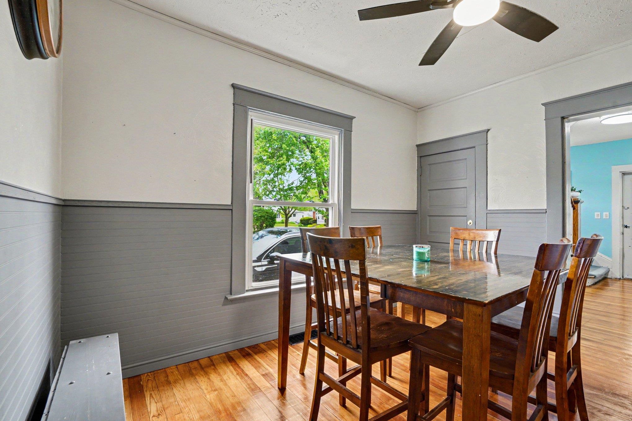 Dining space featuring wood-finish flooring, wainscoting, a ceiling fan with integrated lighting, and a large window