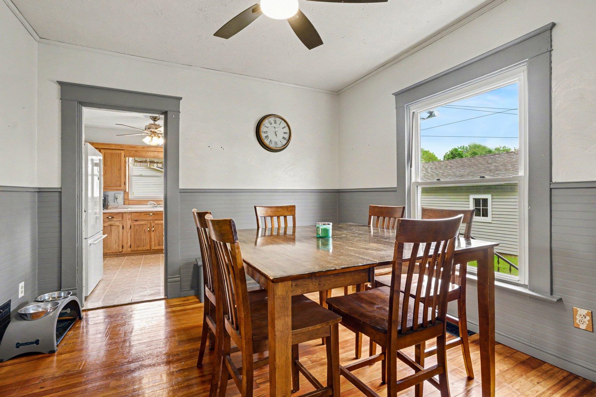 Dining area featuring wood-finish flooring, a ceiling fan with integrated lighting, and a wide window with grey trim