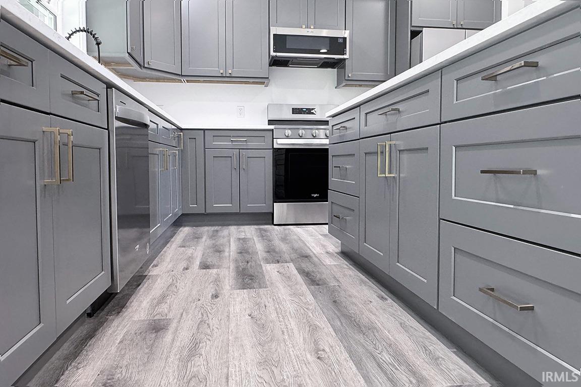 Kitchen featuring grey shaker-style cabinetry with varied hardware, white countertops, and wood-finish flooring