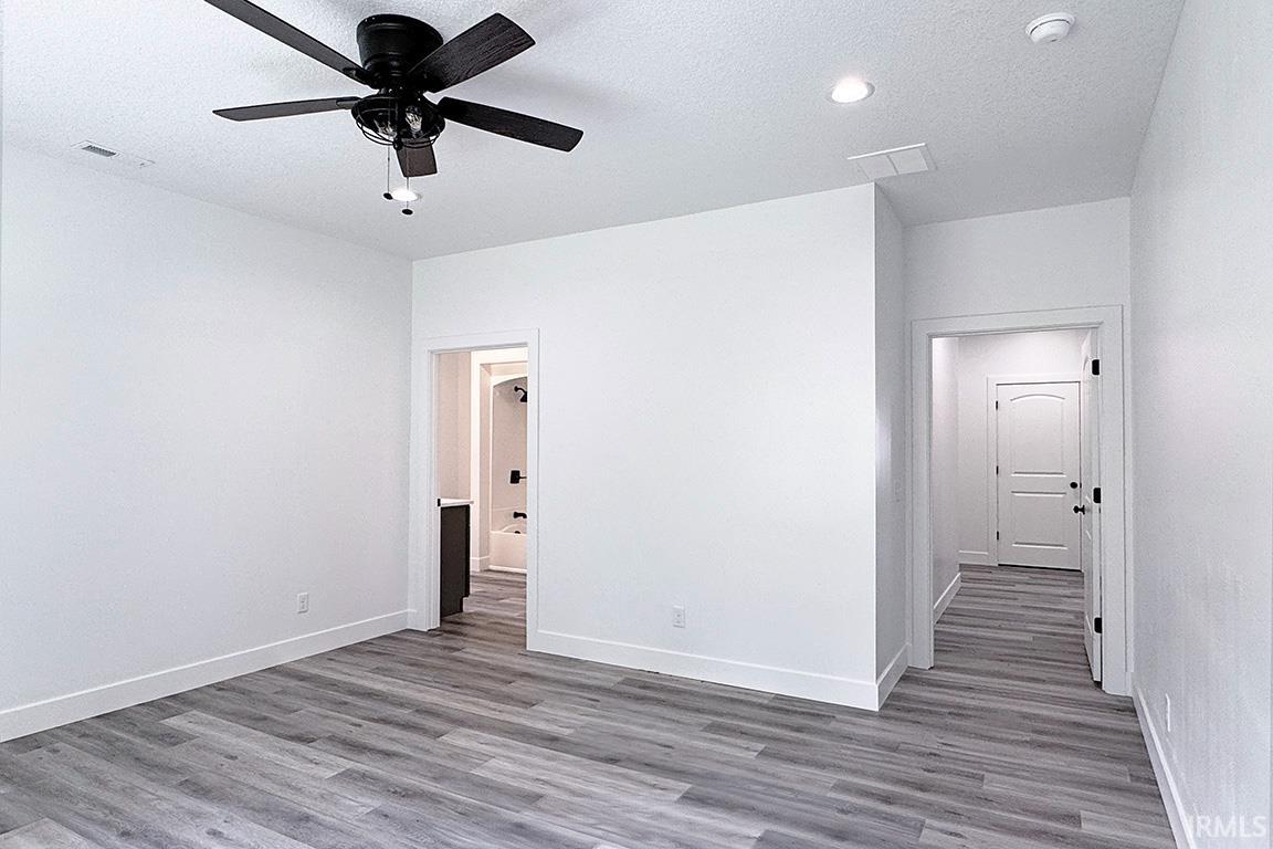 Spacious room featuring wood-finish flooring, a ceiling fan, recessed lighting, and crisp white walls