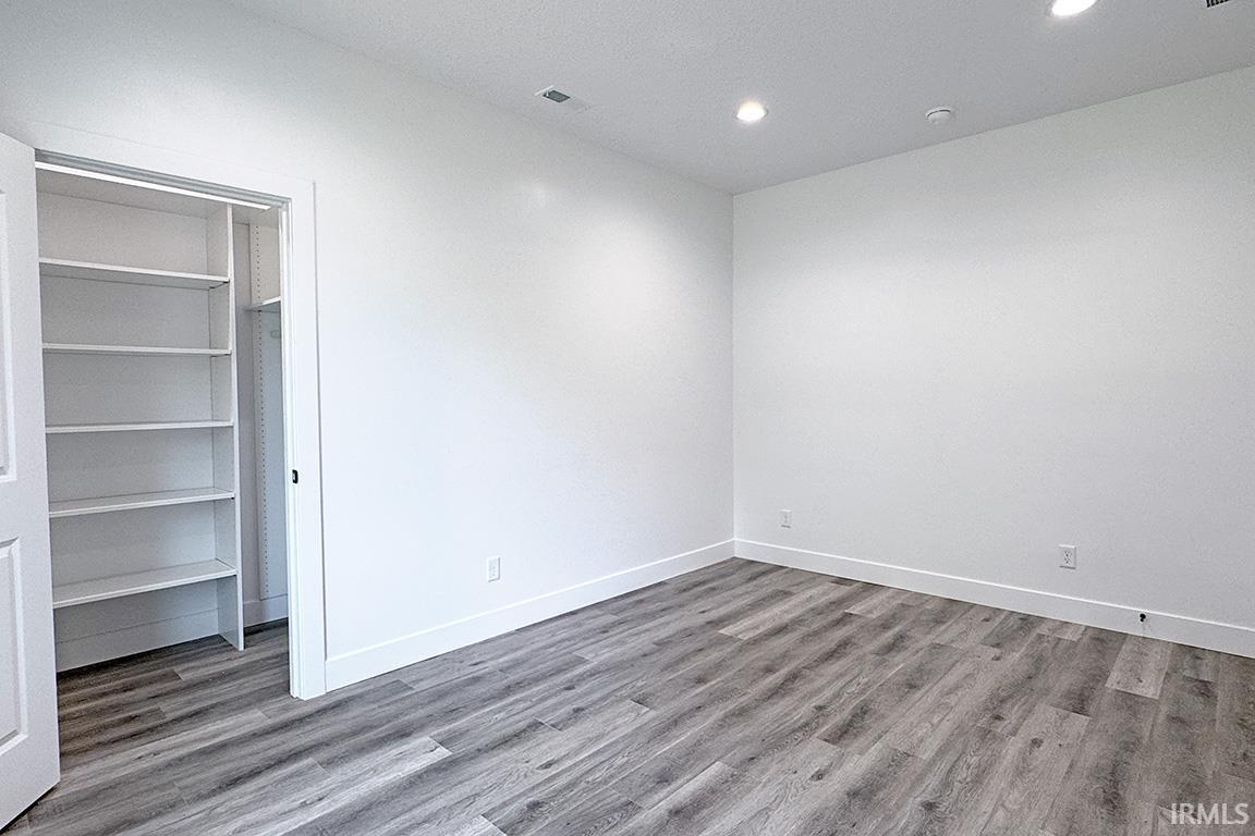 Room featuring wood-finish flooring, white walls, recessed lighting, and a built-in closet with shelving