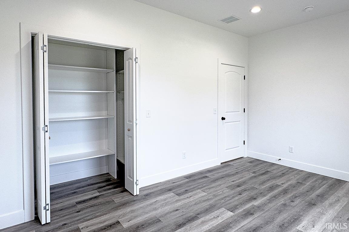 Built-in closet with adjustable shelving, wood-finish flooring, recessed lighting, and white trim molding