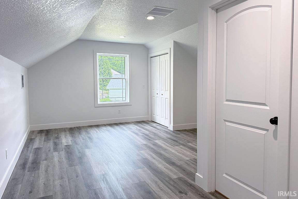 Room featuring wood-finish flooring, a window with exterior visibility, a bi-fold closet door, and a paneled door with an arched top