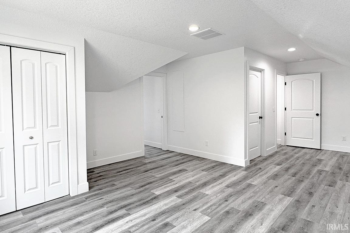 Spacious room featuring wood-finish flooring, white walls, recessed lighting, and multiple white doors with black hardware