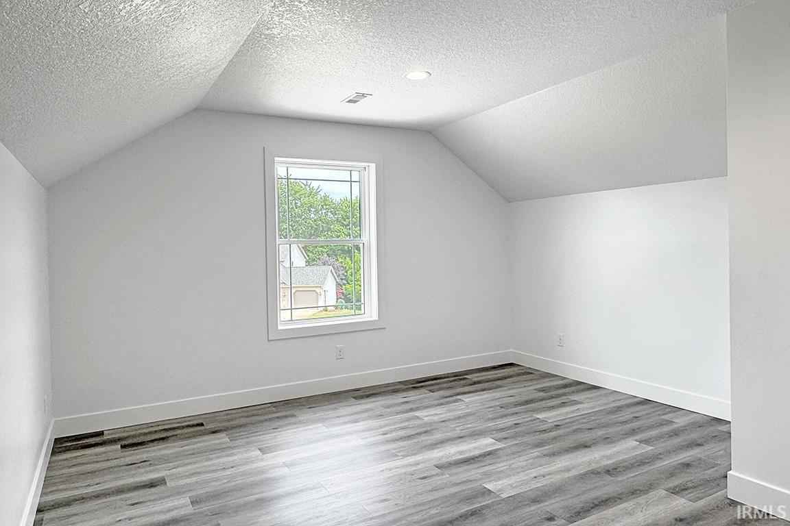 Room featuring vaulted ceilings, wood-finish flooring, recessed lighting, and a double-pane window with grid inserts
