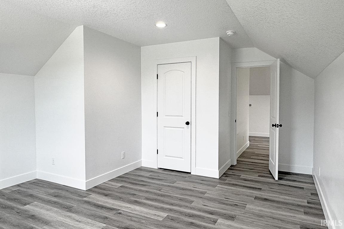 Room featuring sloped ceilings, wood-finish flooring, white trim, and a white paneled door