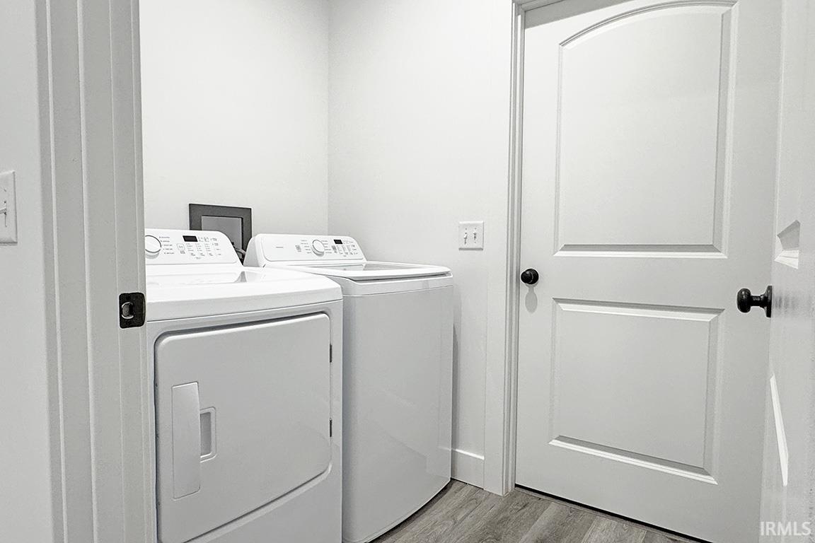 Dedicated laundry area featuring wood-finish flooring, white walls, and a paneled interior door with an arched top