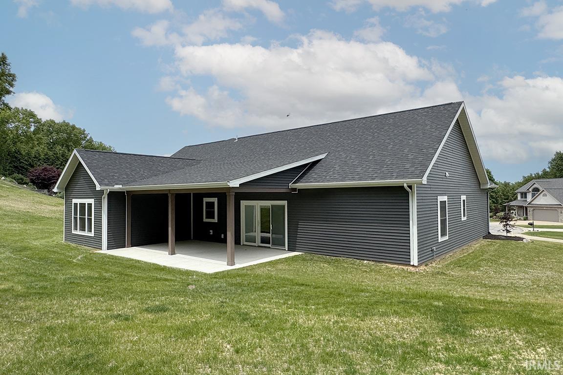 Rear exterior featuring dark horizontal siding, white trim, a covered patio with concrete flooring, support columns, and sliding glass doors
