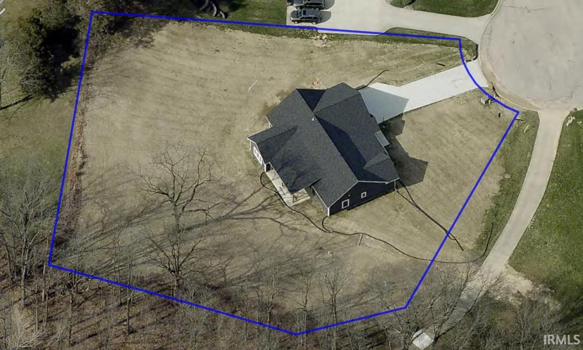 Modern residence featuring a dark gray roof, light-colored driveway, and a spacious lot with mature trees