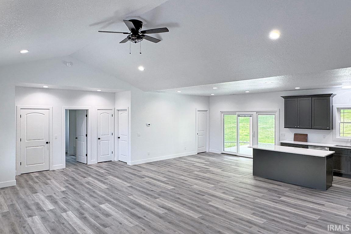 Open-concept living area featuring vaulted ceilings, recessed lighting, wood-finish flooring, a ceiling fan, and a kitchen island with stone countertops