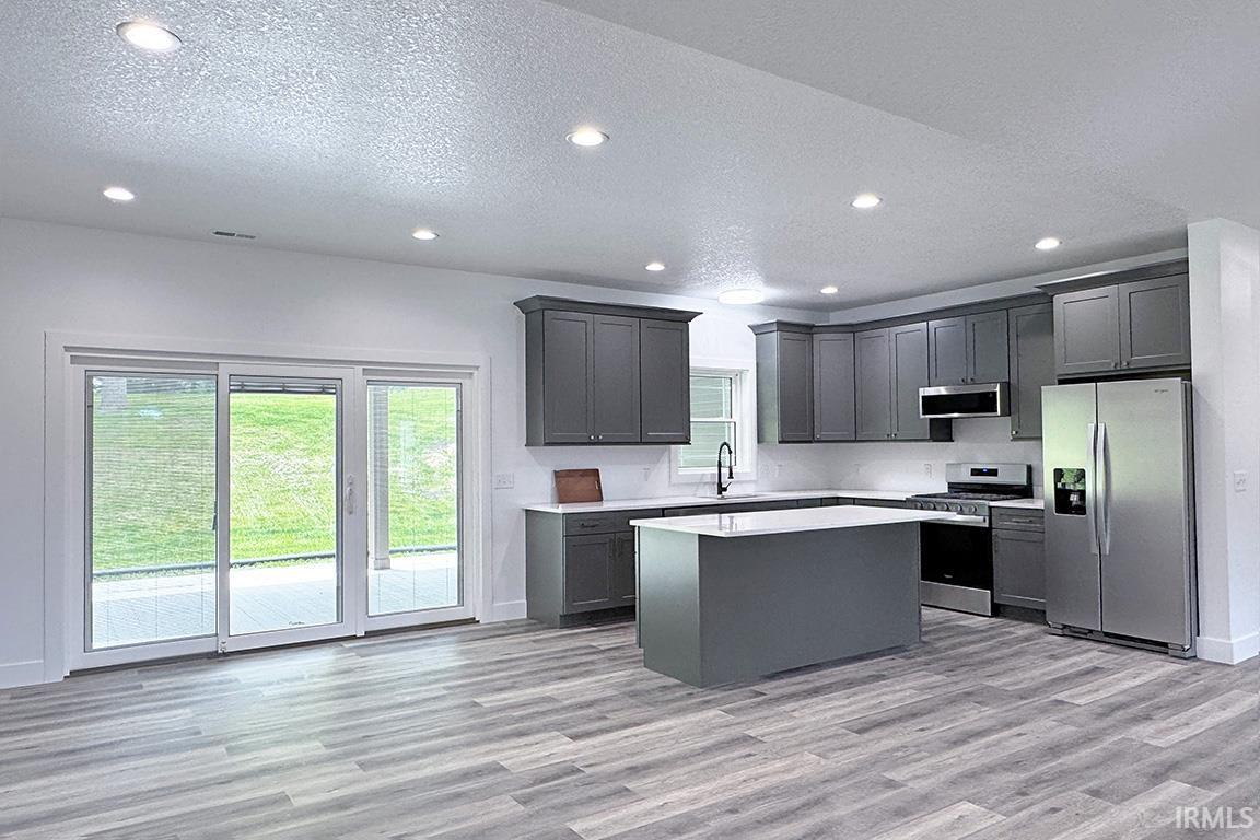 Kitchen featuring gray cabinetry, a central island, white countertops, stainless steel appliances, and wood-finish flooring