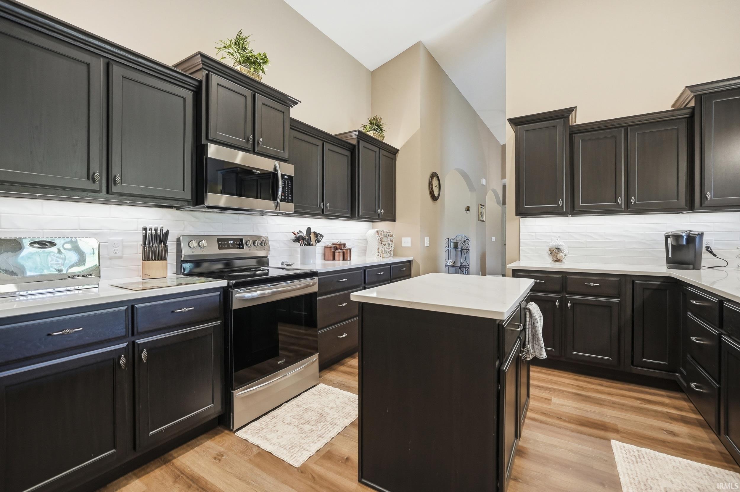 Kitchen featuring dark cabinetry, light countertops, wood-finish flooring, stainless steel appliances, and a central island