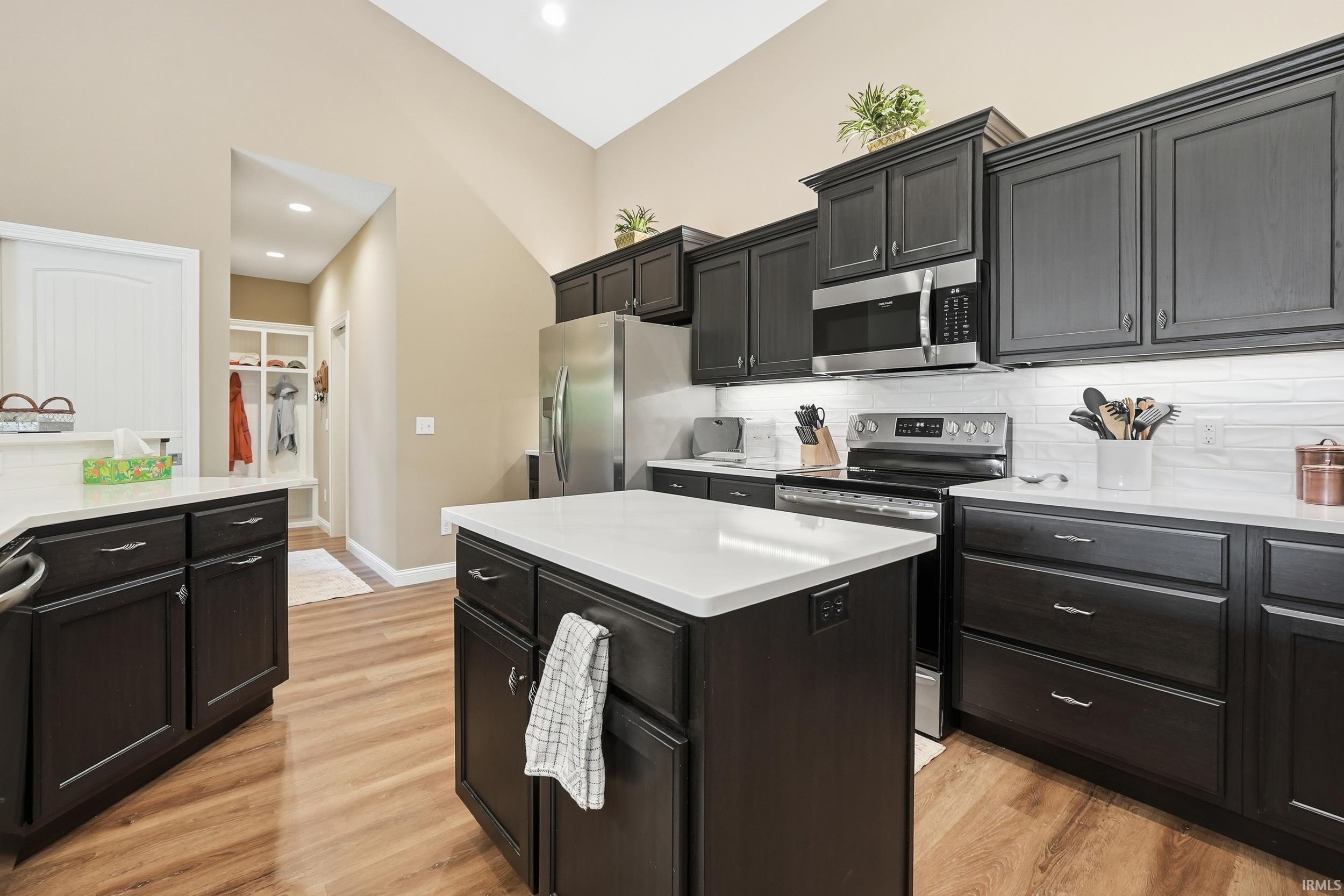 Kitchen featuring dark cabinetry, white countertops, stainless steel appliances, wood-finish flooring, and a vaulted ceiling