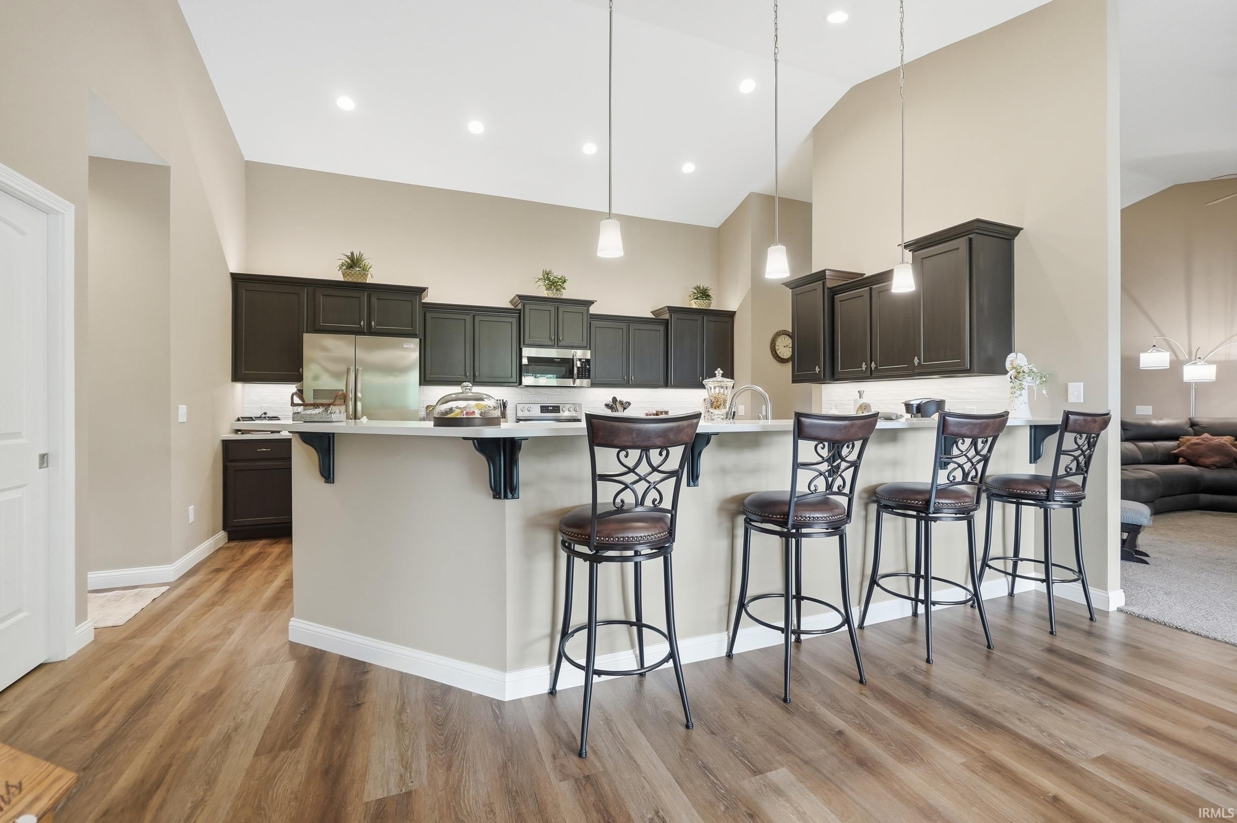 Kitchen featuring dark cabinetry, stainless steel appliances, a breakfast bar, wood-finish flooring, and pendant lighting