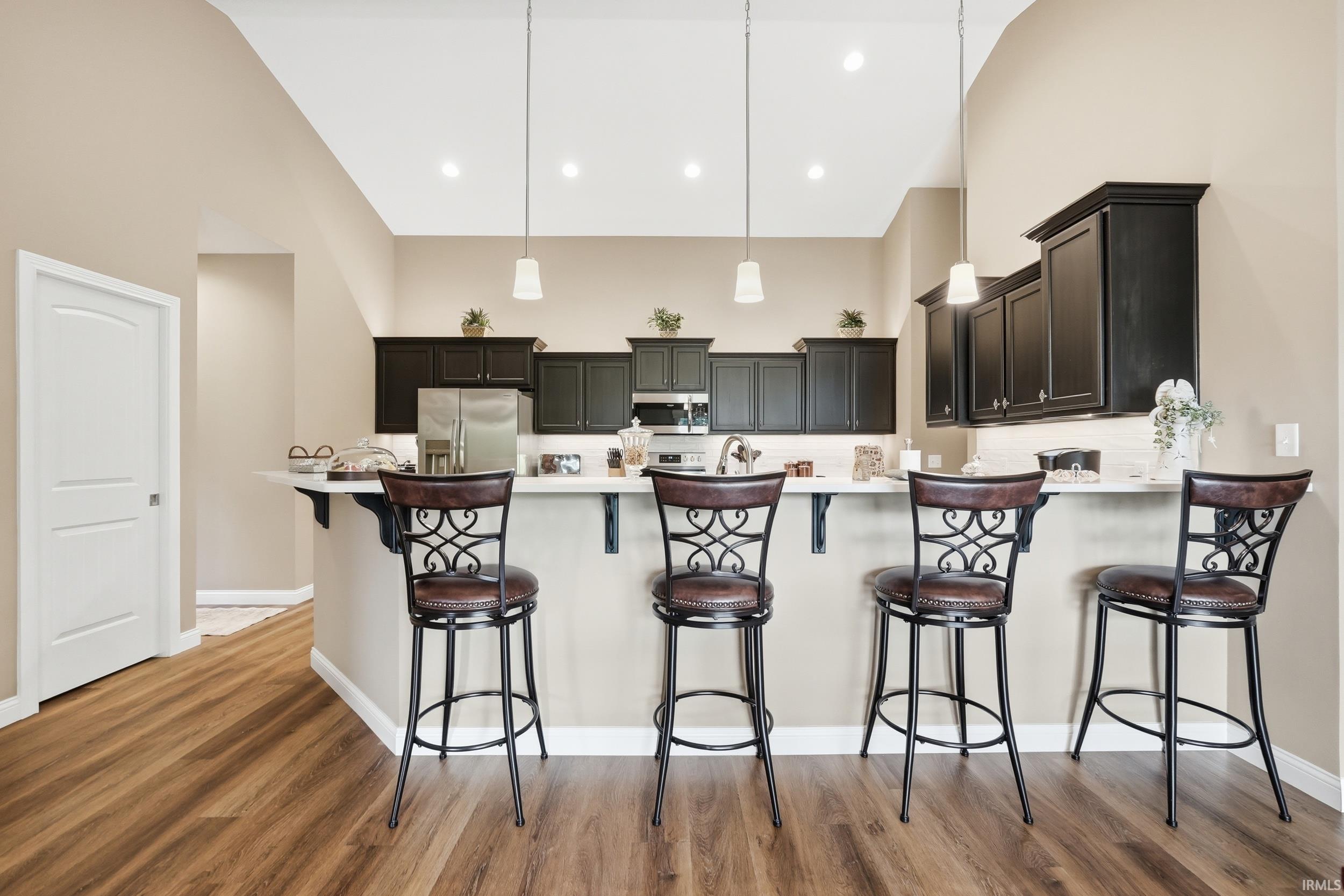 Kitchen featuring an eat-at island with a white countertop, dark wood-finish cabinetry, stainless steel appliances, and a tile backsplash