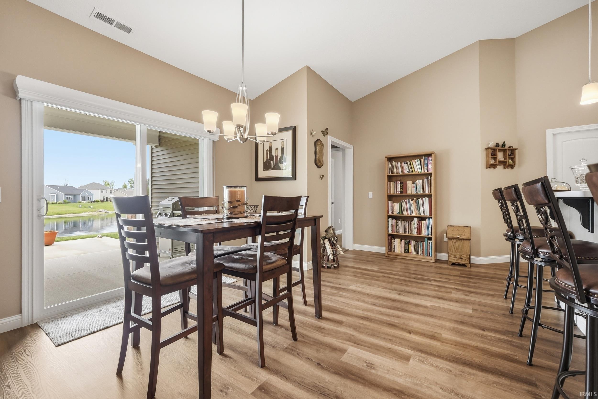 Vaulted ceiling dining area featuring wood-finish flooring, a contemporary chandelier, and sliding glass doors opening to a concrete patio with water frontage