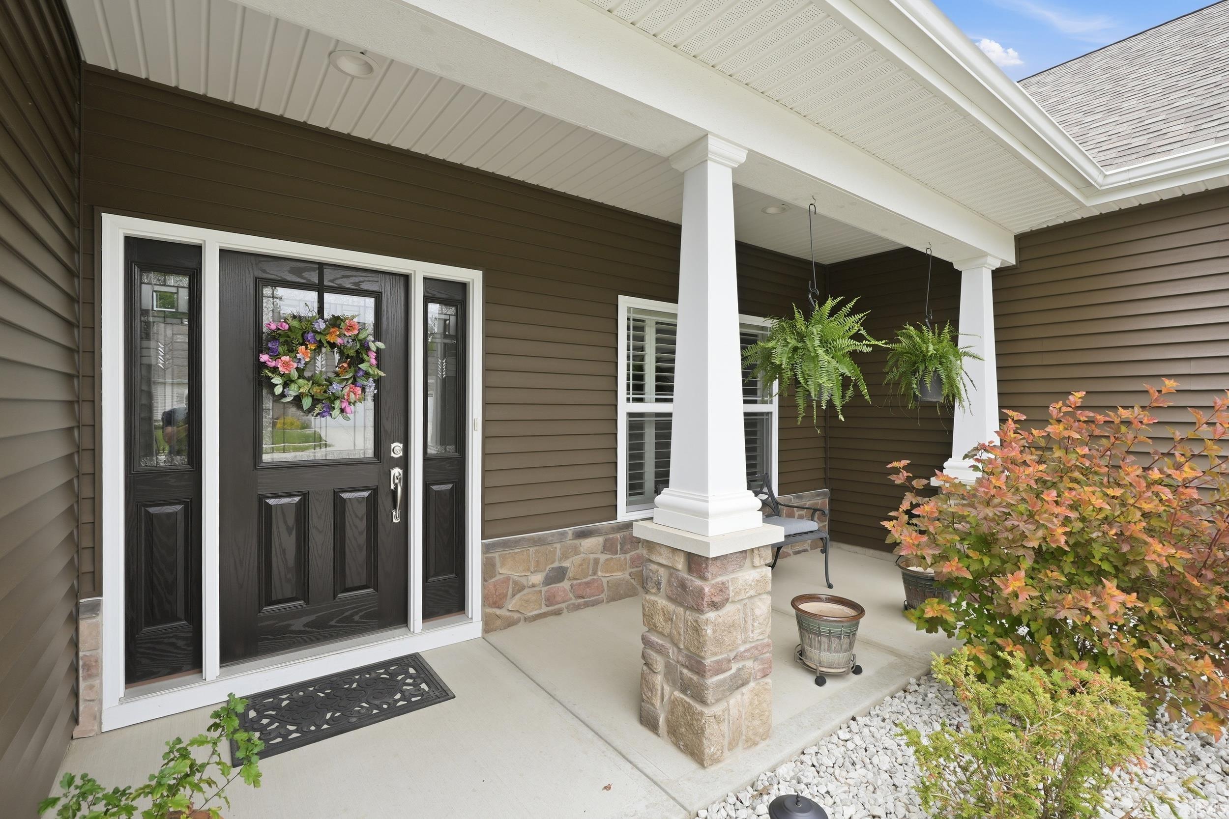Covered front porch featuring a dark brown wood-finish entry door with clear glass inserts, flanked by matching sidelights