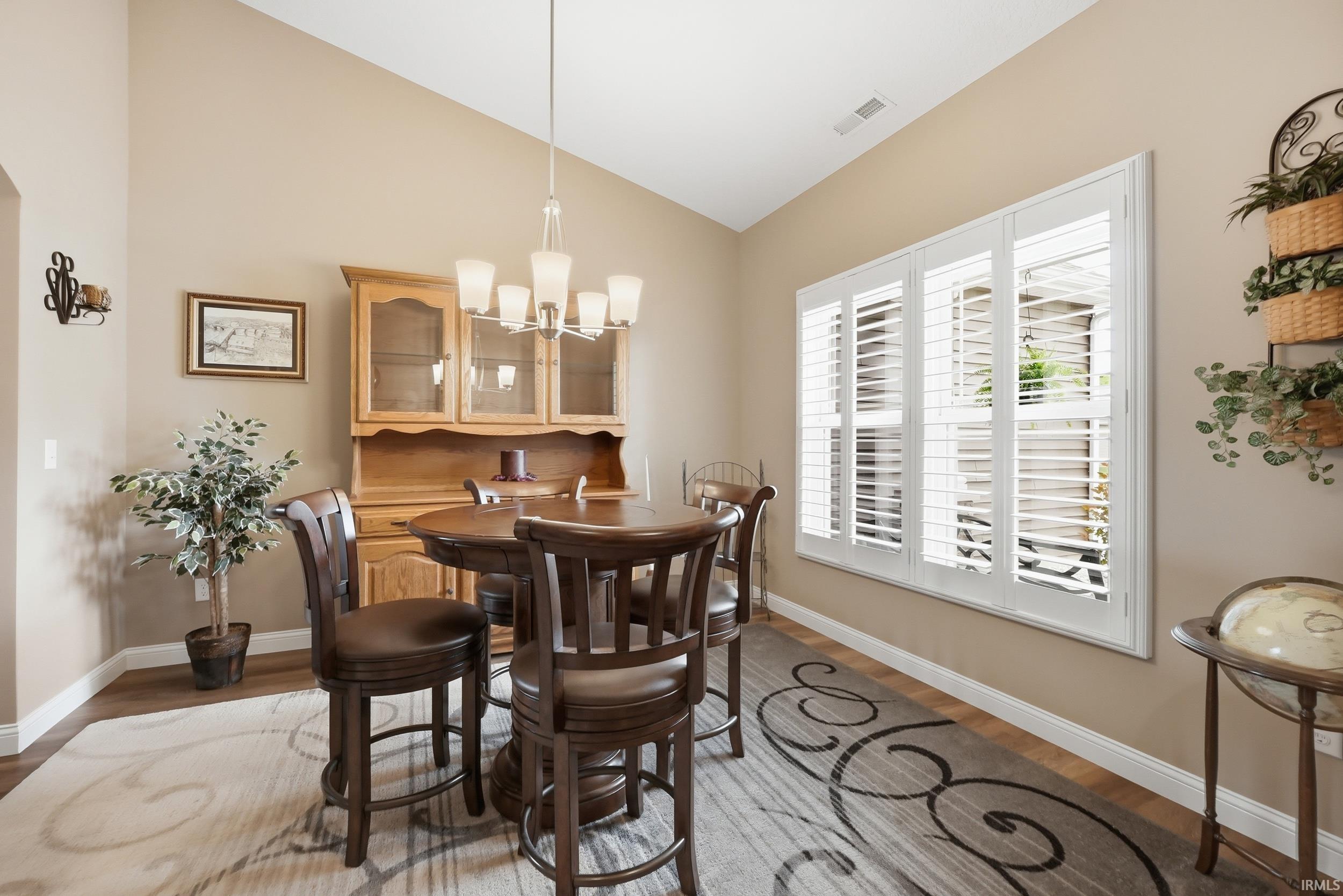 Vaulted ceiling, wood-finish flooring, and a large window with white plantation shutters