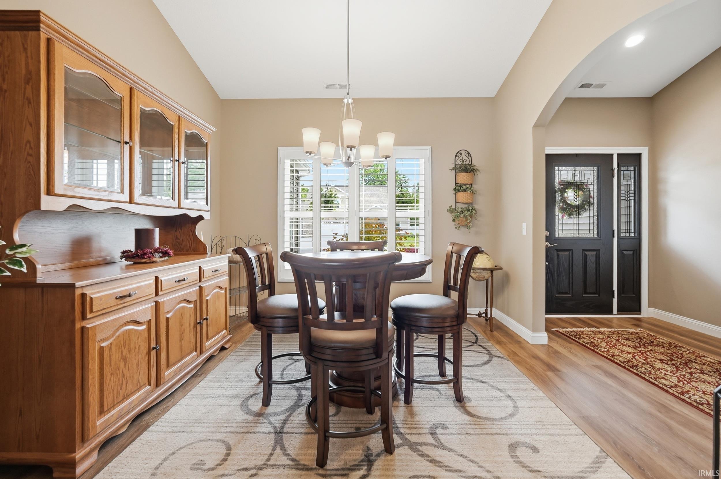 Vaulted ceiling dining area featuring wood-finish flooring, a contemporary chandelier, and a large window with plantation shutters