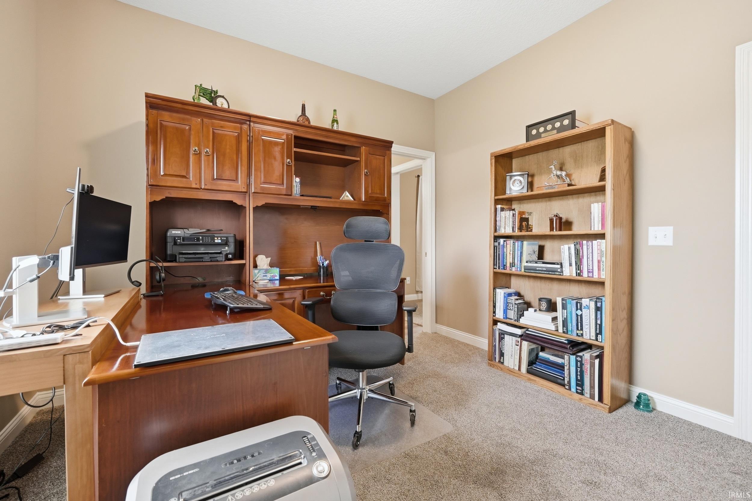 Carpeted room with neutral-toned walls, featuring a built-in wood-finish office hutch with cabinet storage and shelving