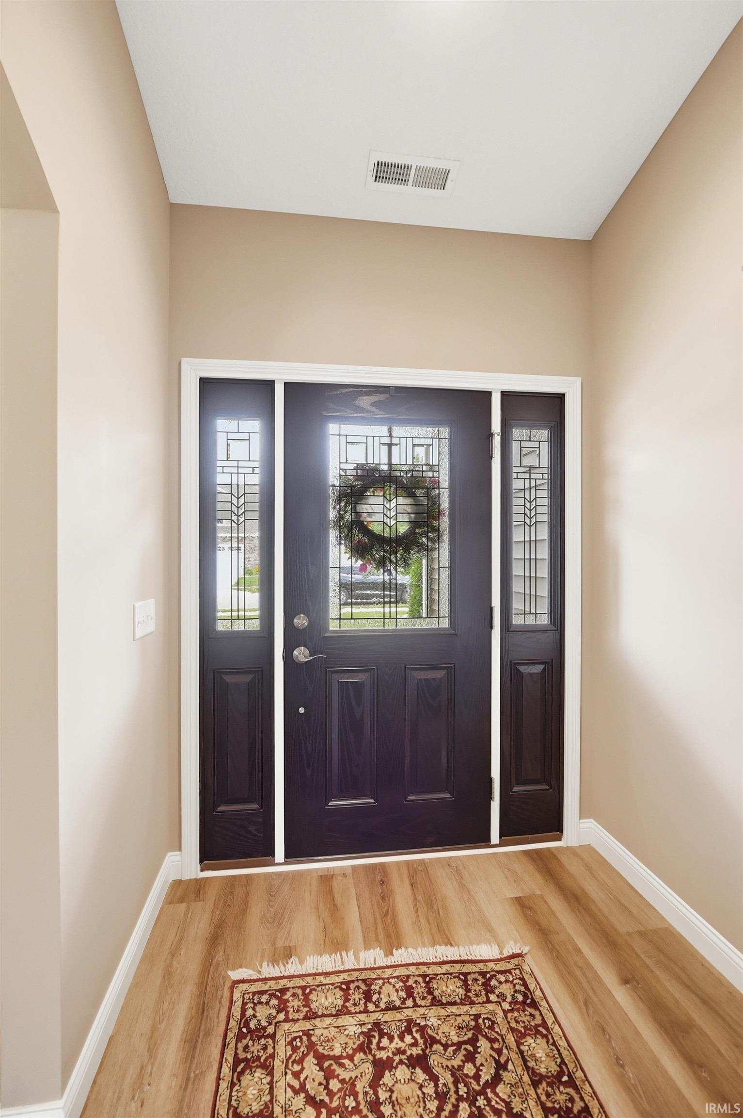 Entryway featuring a dark wood-finish door with decorative glass inserts, two sidelight windows with matching decorative glass, and light wood-finish flooring