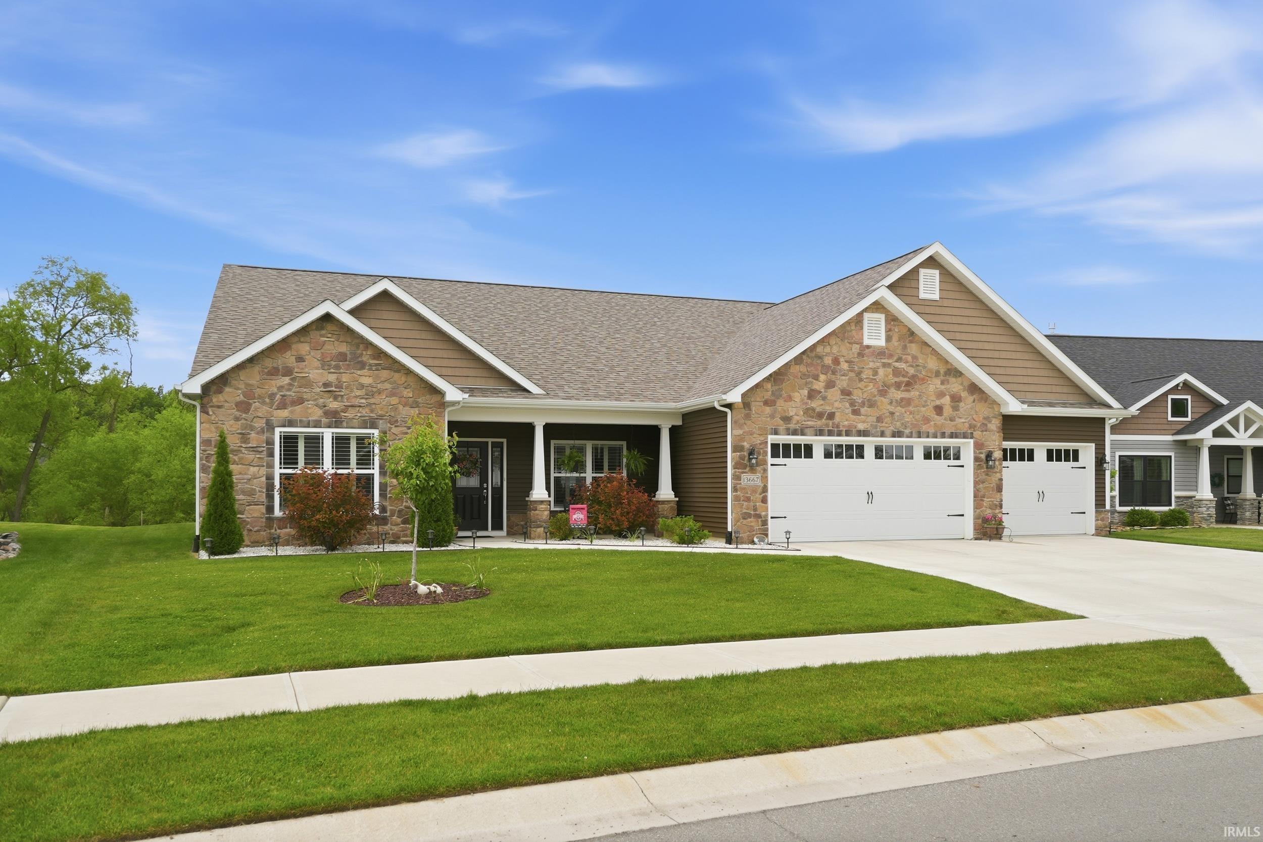Ranch-style residence featuring a stone and siding exterior, an inviting covered front porch with white columns, a meticulously maintained front lawn, and a two-car garage with panel doors