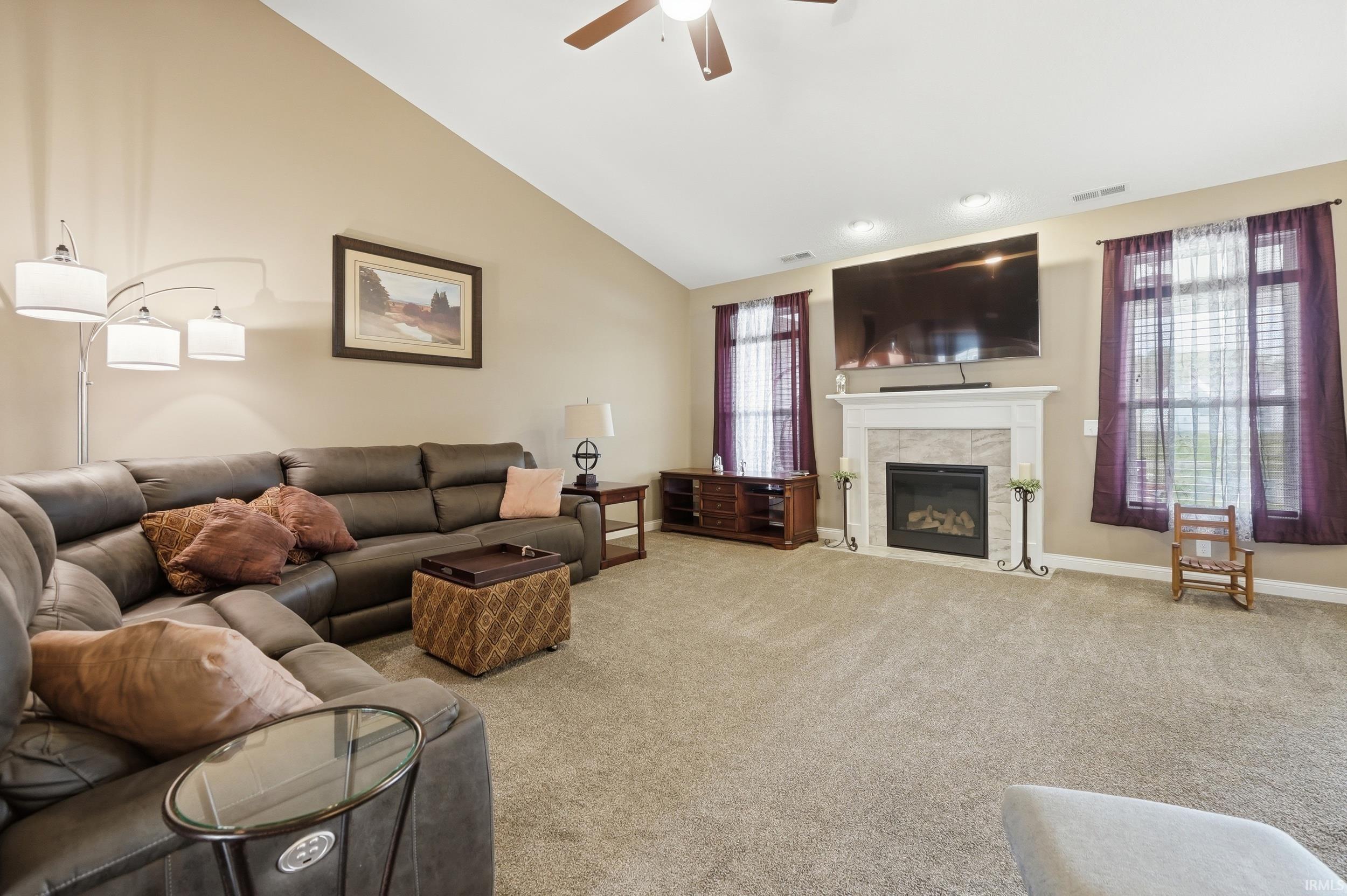 Spacious living area featuring a vaulted ceiling, neutral carpeting, and a fireplace with a mantel