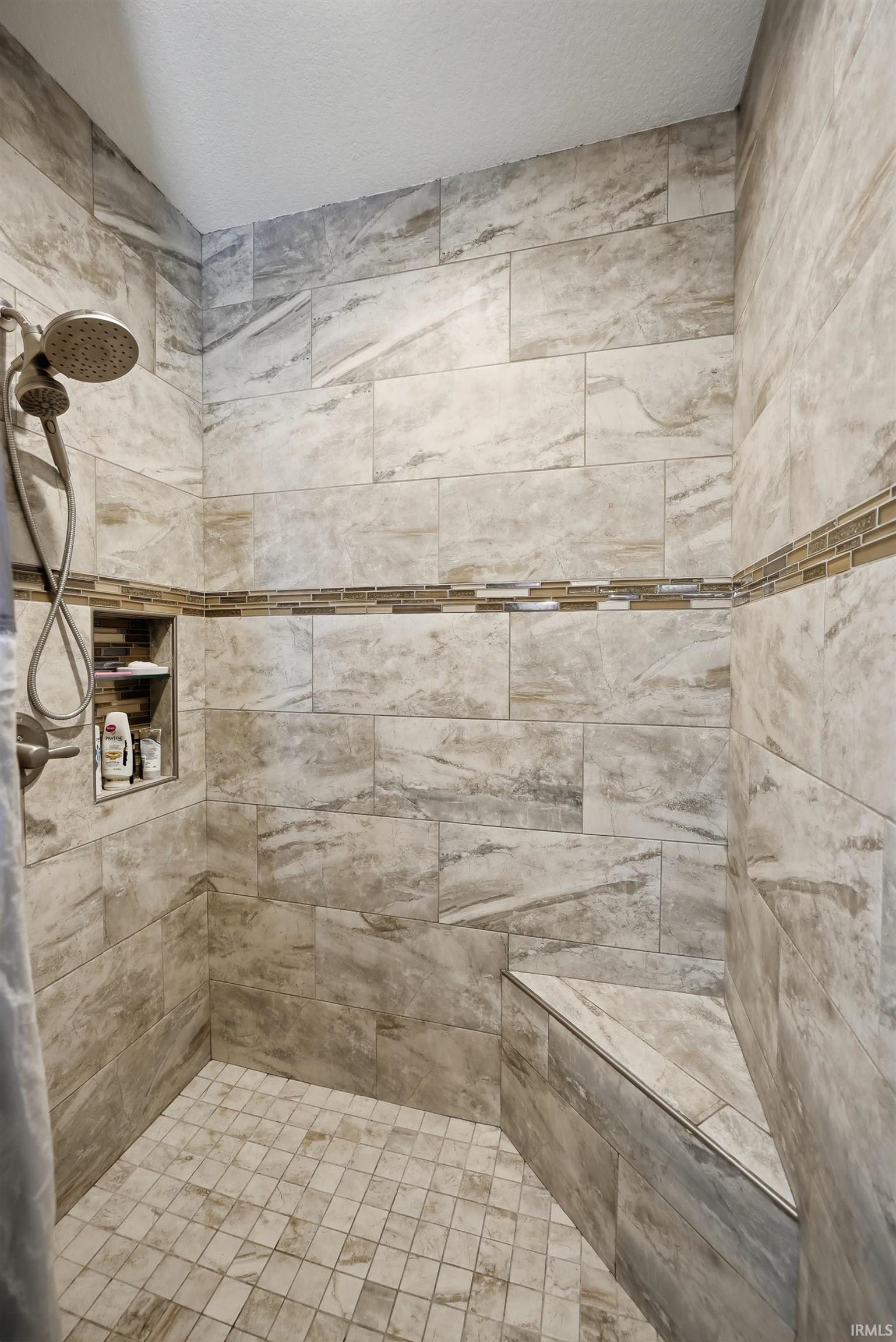 Tiled shower featuring a built-in bench, recessed niche, decorative glass tile accent band, and a multi-function showerhead