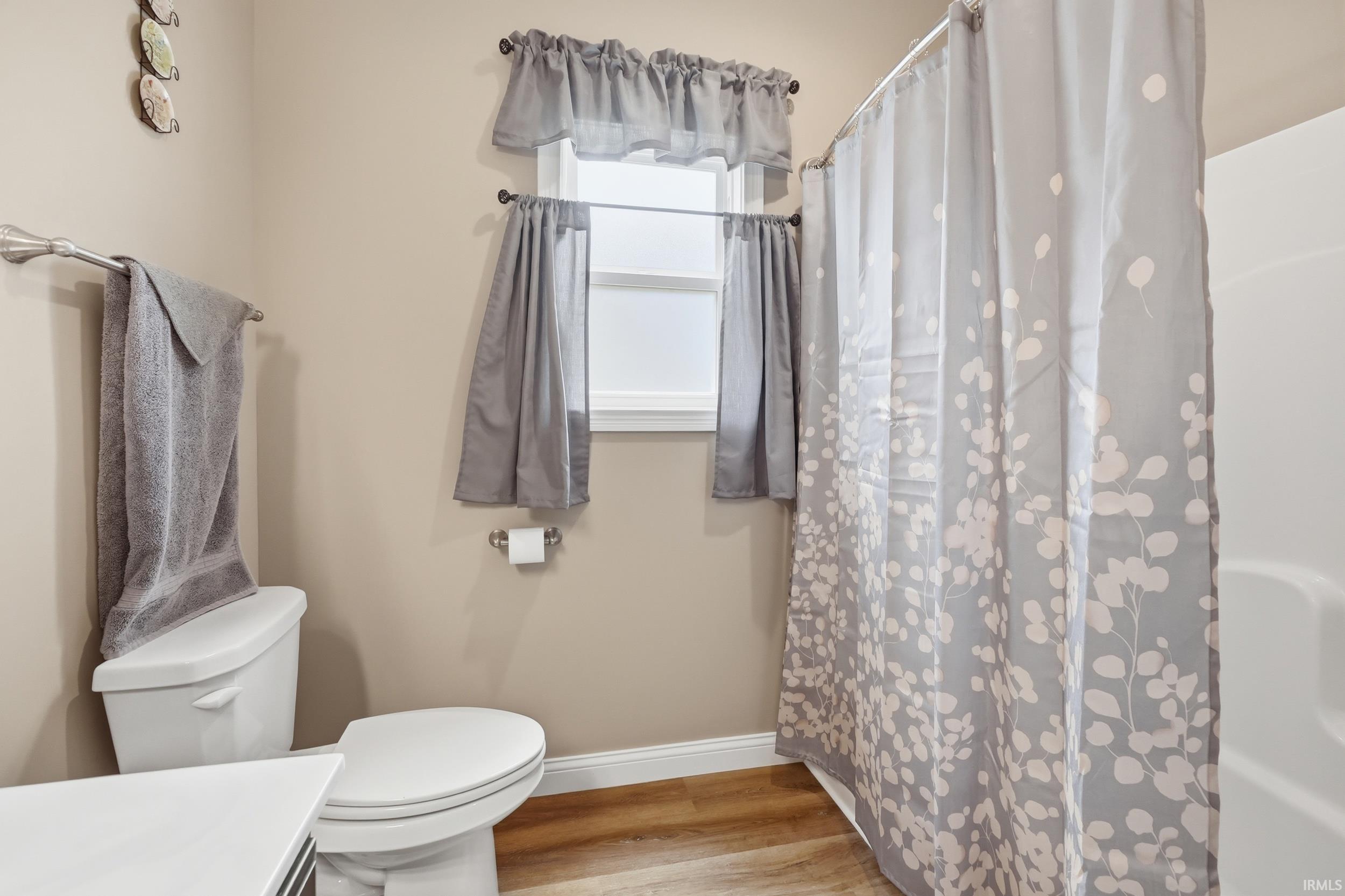 Bathroom with wood-finish flooring, a white toilet, and a window with white trim