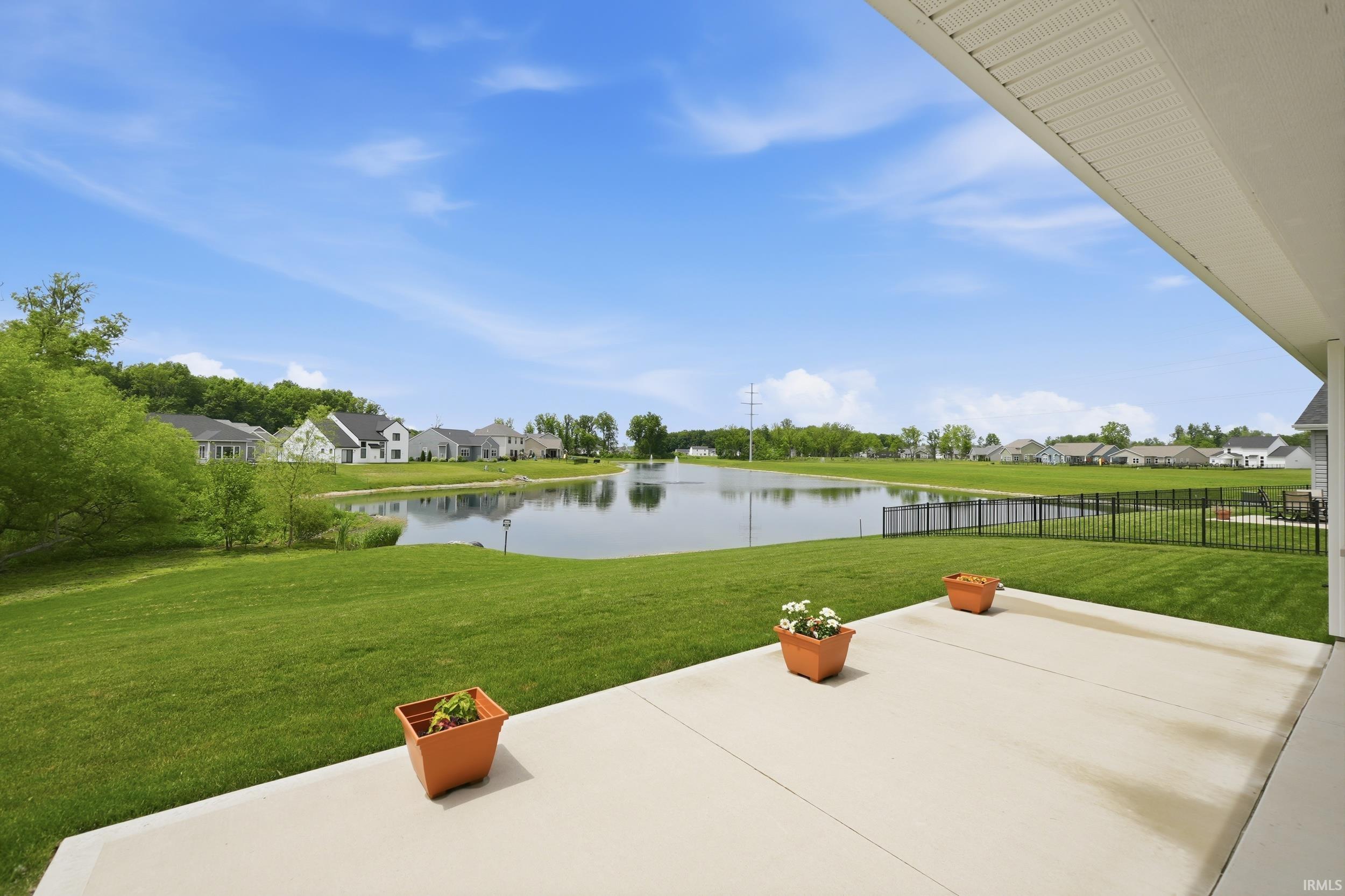 Patio area featuring a concrete surface, expansive green lawn, and a black metal fence enclosing the property boundary