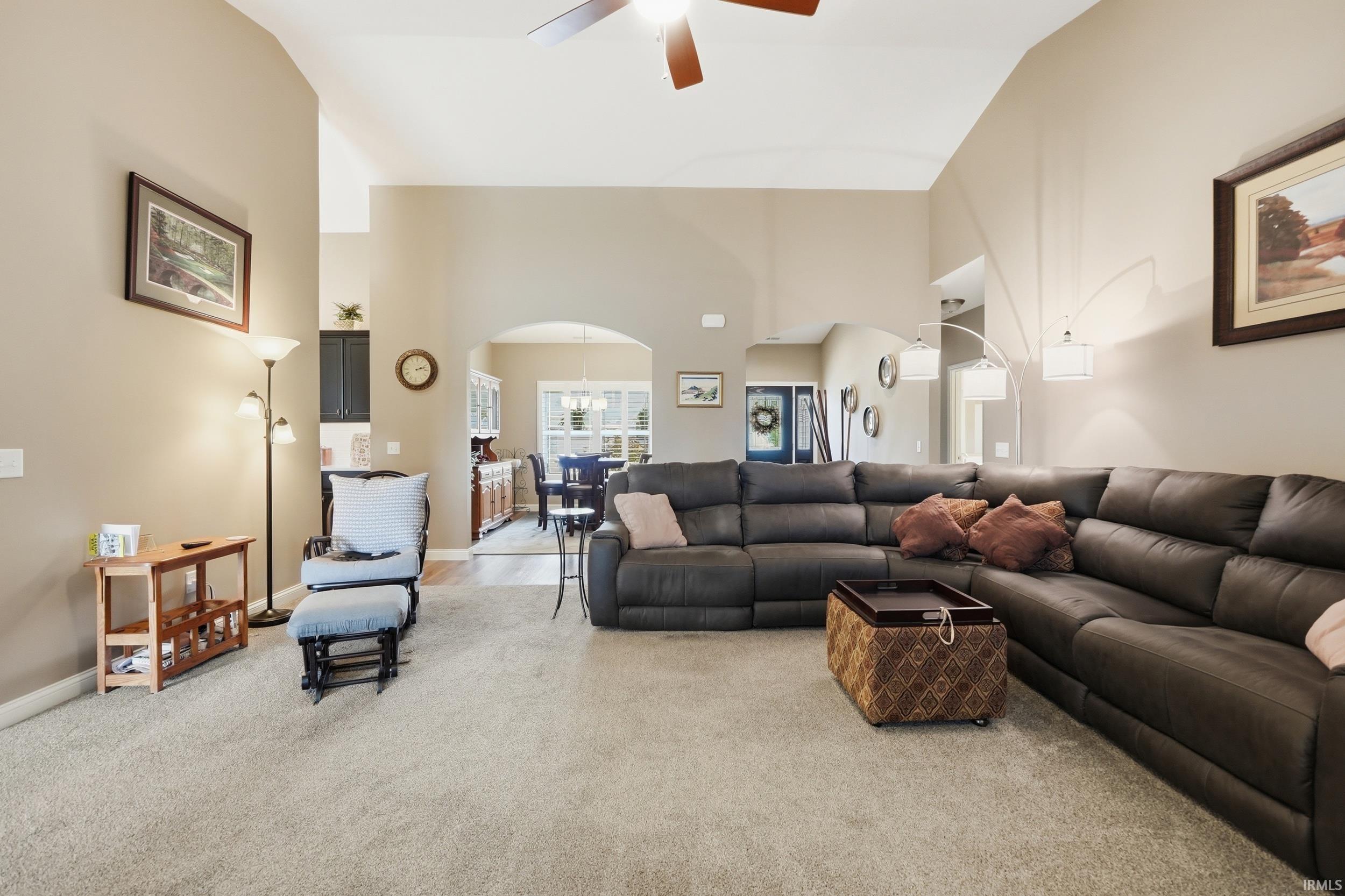 Spacious living area featuring vaulted ceilings, light-toned carpeting, and a ceiling fan