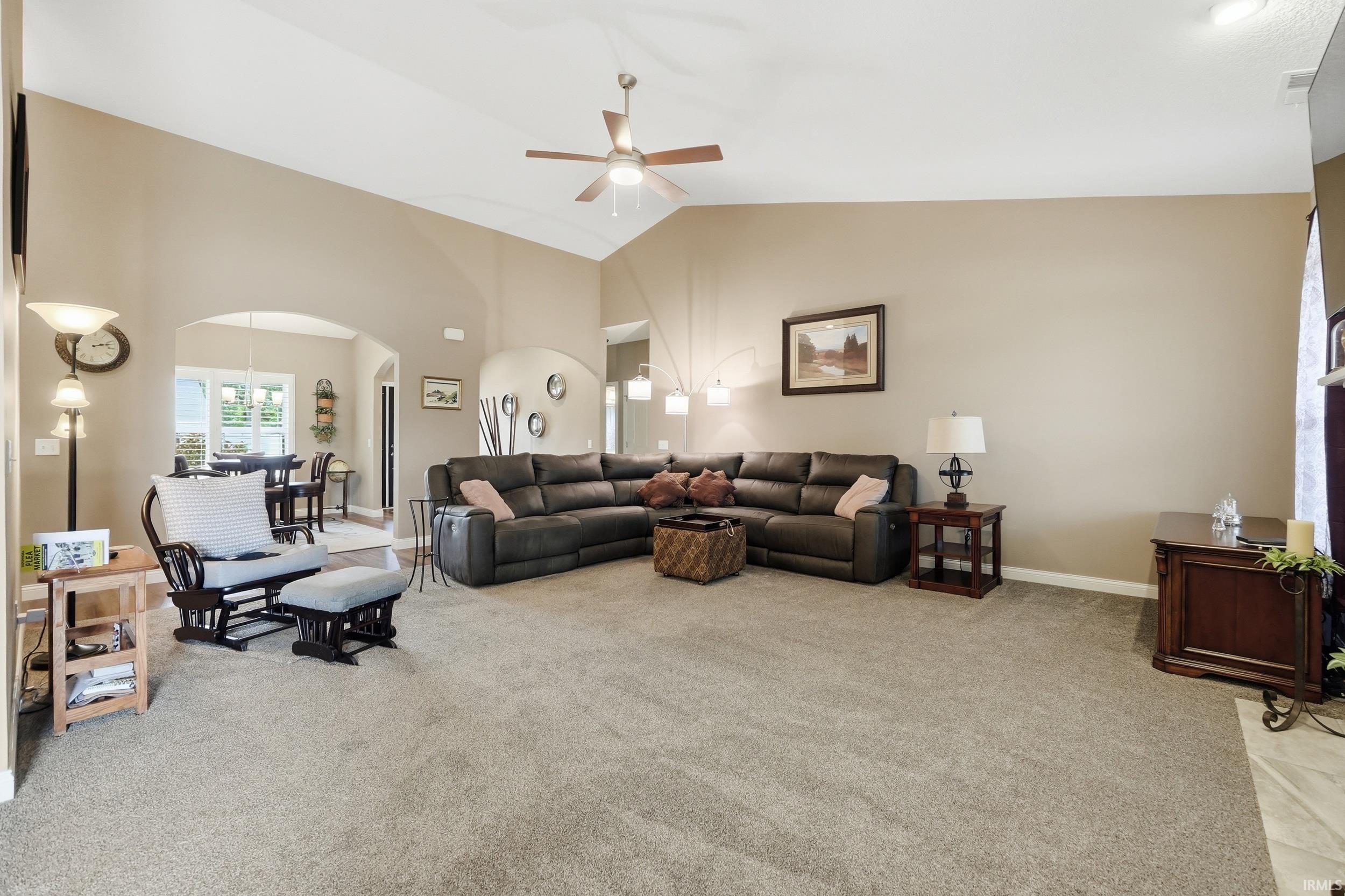 Spacious living area featuring vaulted ceilings, a ceiling fan, and neutral-toned wall paint