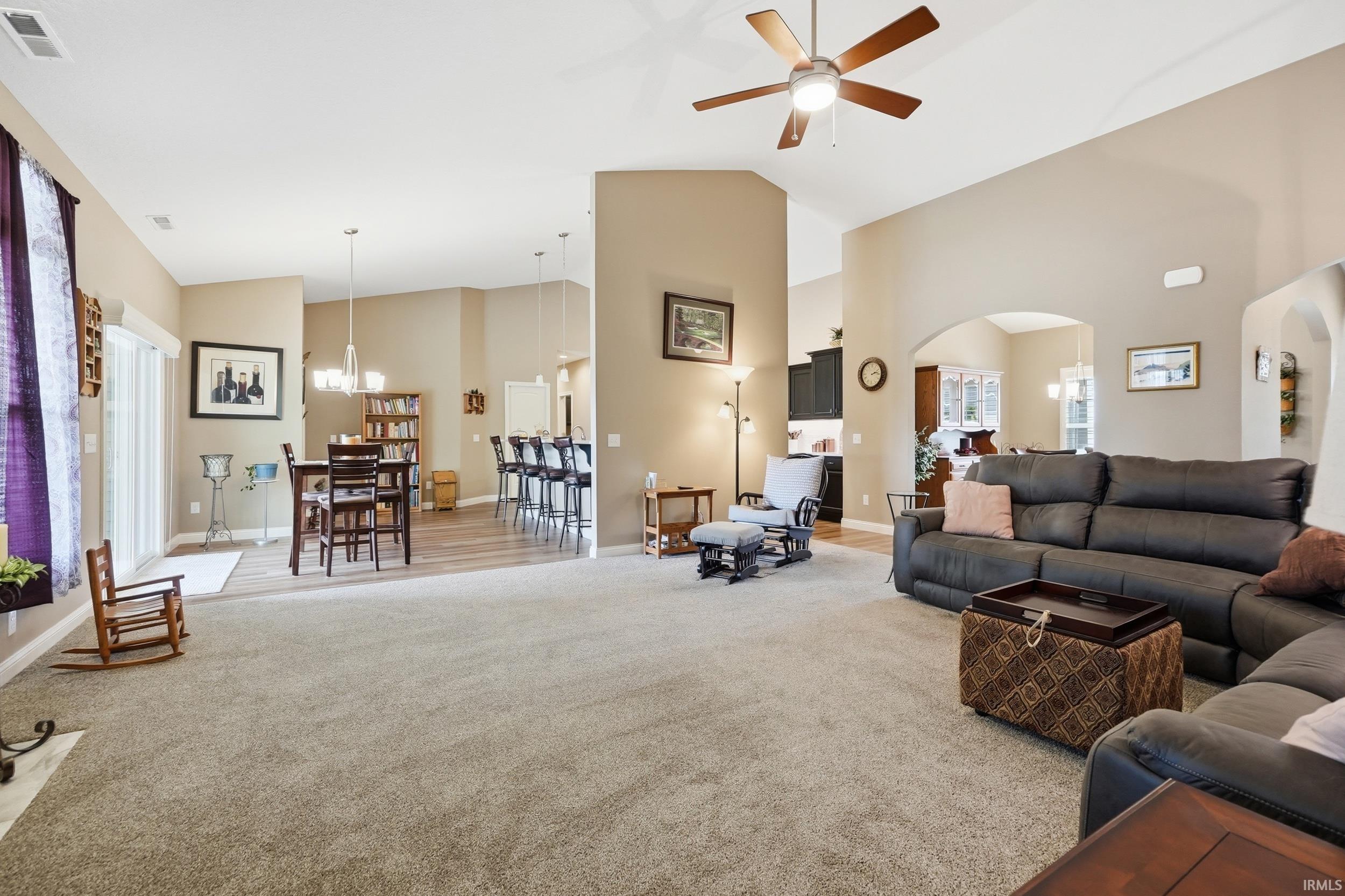 Spacious living area featuring vaulted ceilings, a ceiling fan, and carpeted flooring